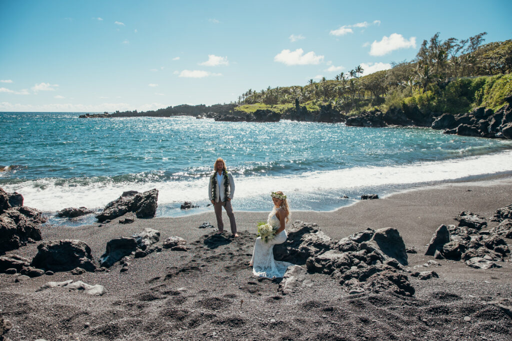 Maui Elopement Photographer captures bride and groom on beach sitting on rock and standing by water during bridal portraits