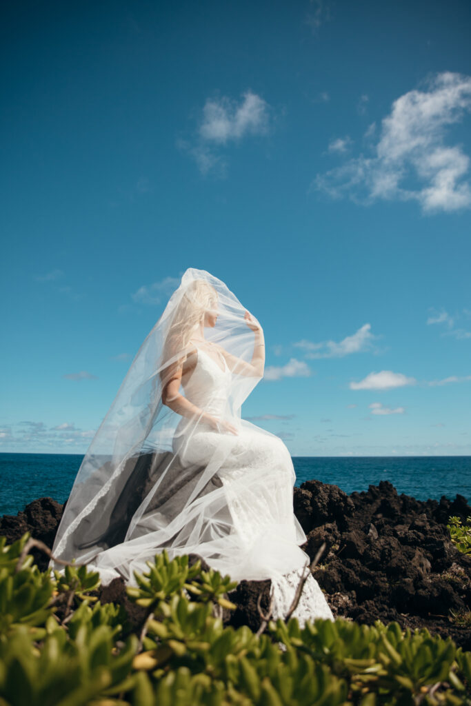 Maui Elopement Photographer captures bride sitting on rock with veil over face