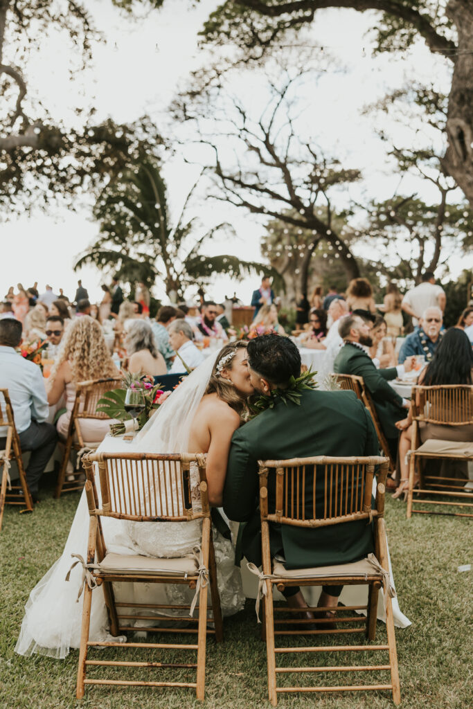 Maui Elopement Photographer captures bride and groom kissing at table during wedding reception