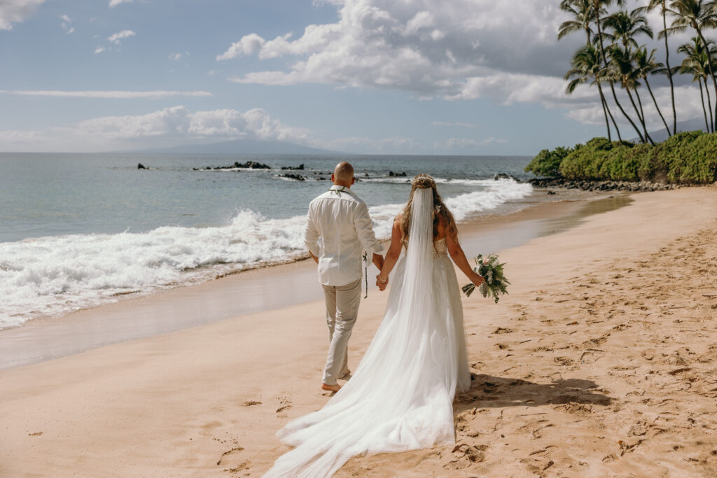 Maui Elopement Photographer captures bride and groom holding hands while walking on the beach