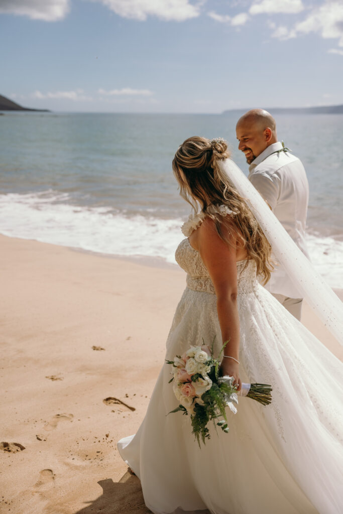 Maui Elopement Photographer captures bride walking on beach with bouquet in hand with husband