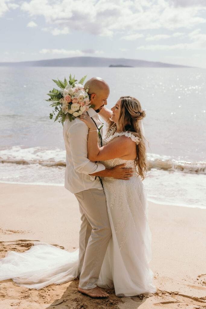 Maui Elopement Photographer captures bride and groom embracing on beach while ocean waves crash