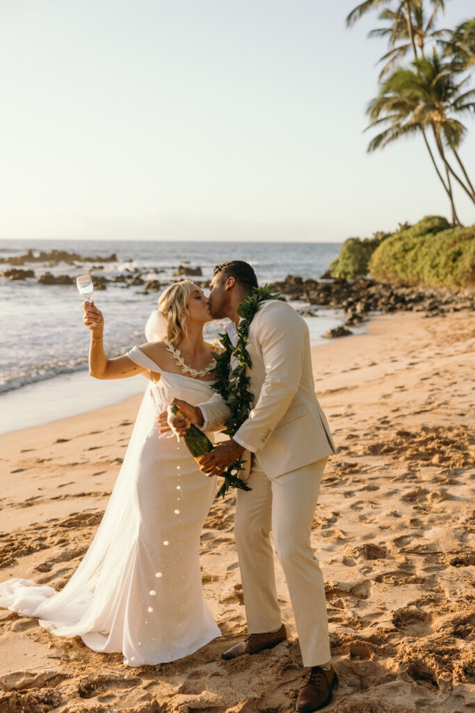 Maui Wedding Photographer captures couple celebrating recent Hawaii beach wedding by popping champagne