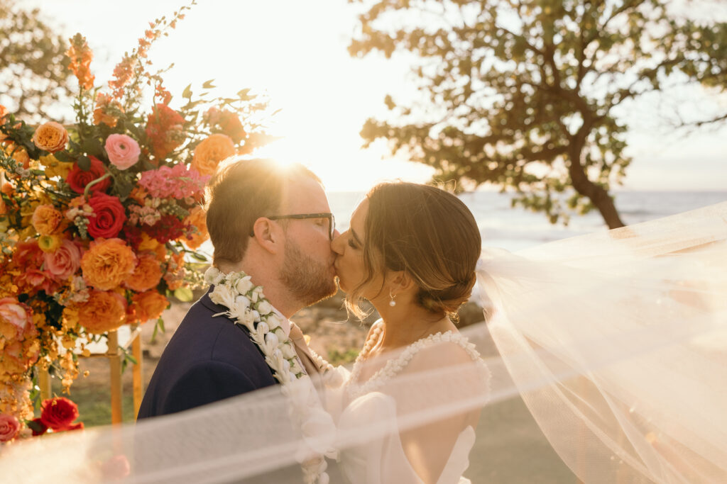 Maui Elopement Photographer captures bride and groom kissing while veil blows in the wind