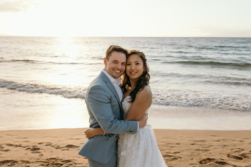 Newlyweds embrace on a sandy beach at sunset, glowing with joy after their Hawaii elopement.

