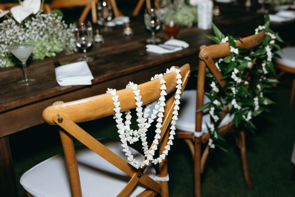 Close-up of wooden wedding chairs adorned with fresh leis and tropical greenery.