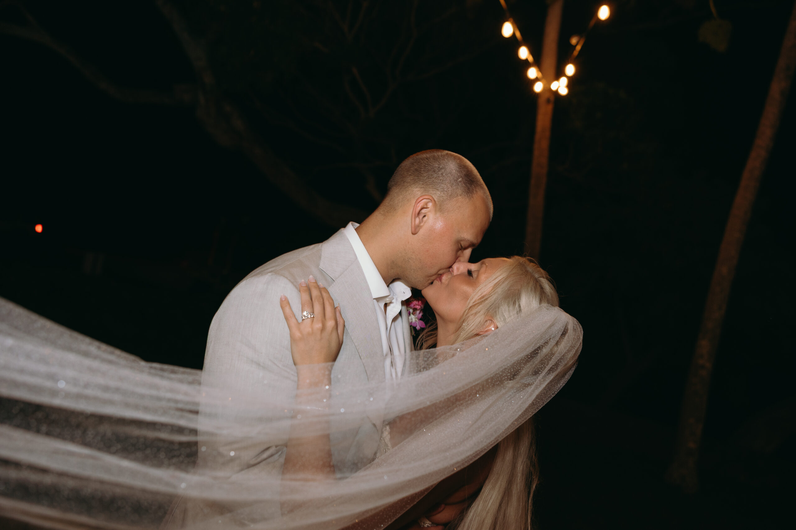 Under a blanket of stars, a groom dips his bride for a kiss as her veil swirls around them—Hawaii wedding planning ending in romantic perfection.