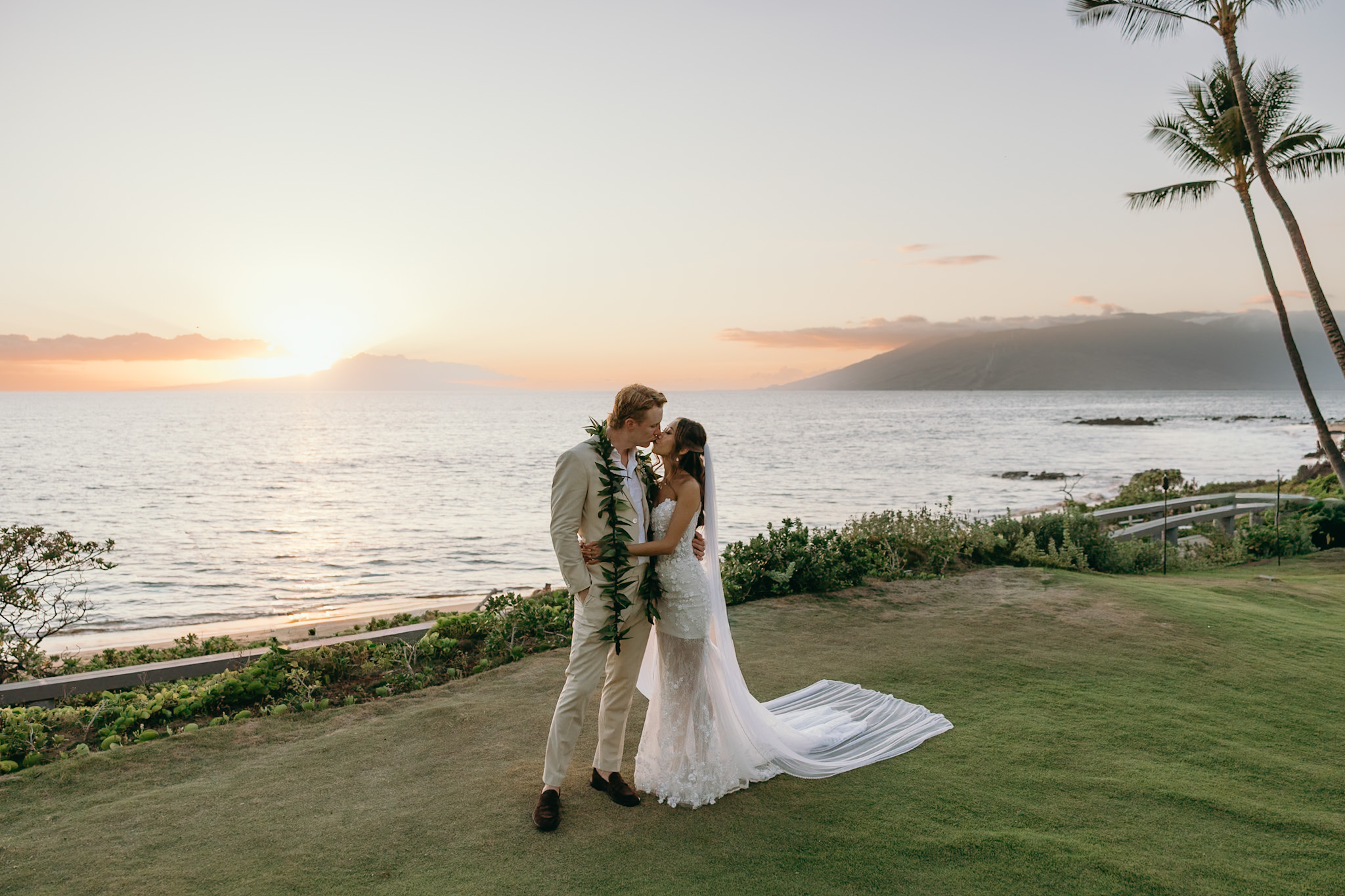 Just married and glowing at golden hour, a couple shares a romantic kiss against the ocean horizon—an unforgettable chapter in their Hawaii wedding planning journey.
