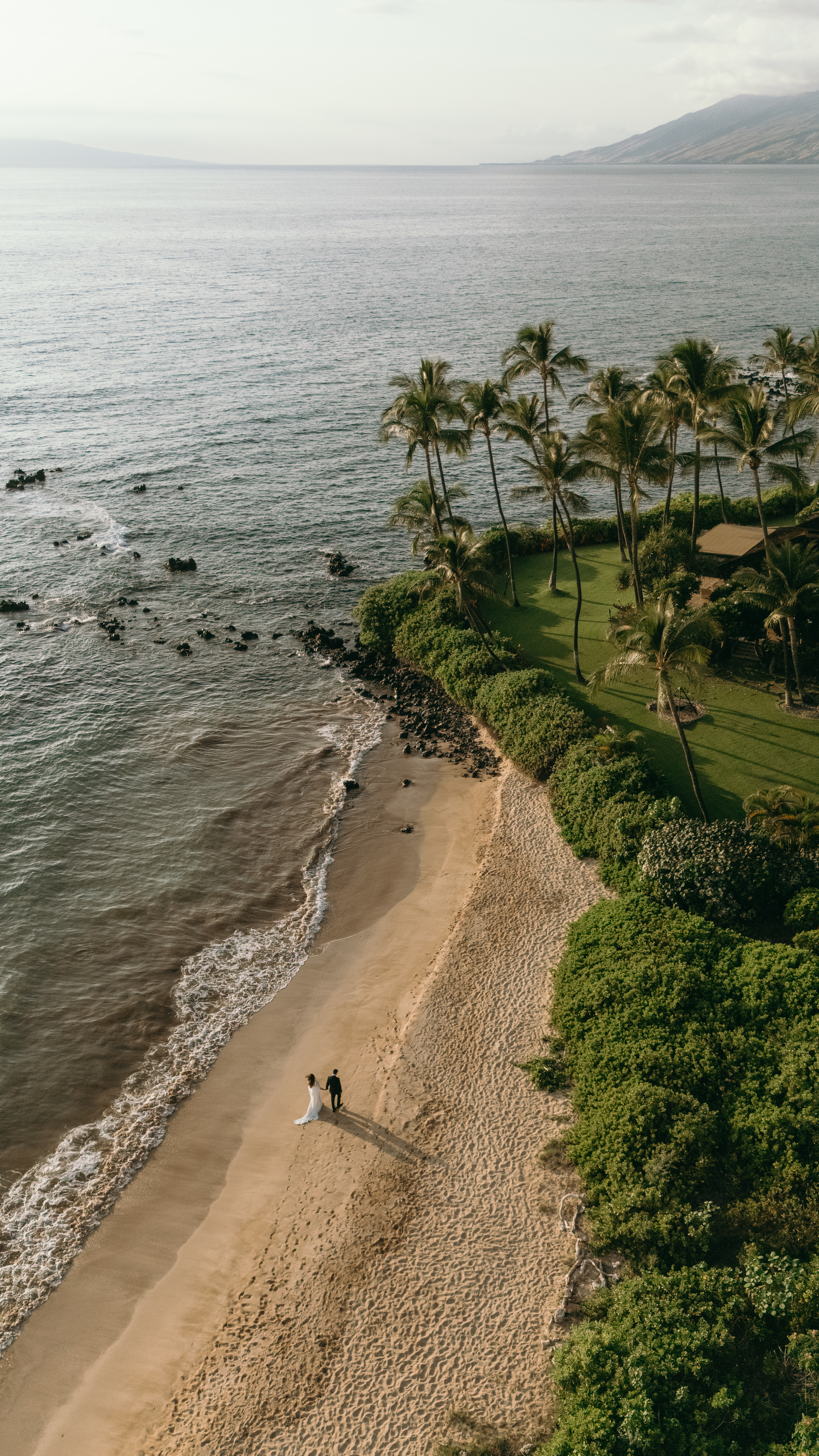 Aerial view of a couple walking along a secluded beach at golden hour