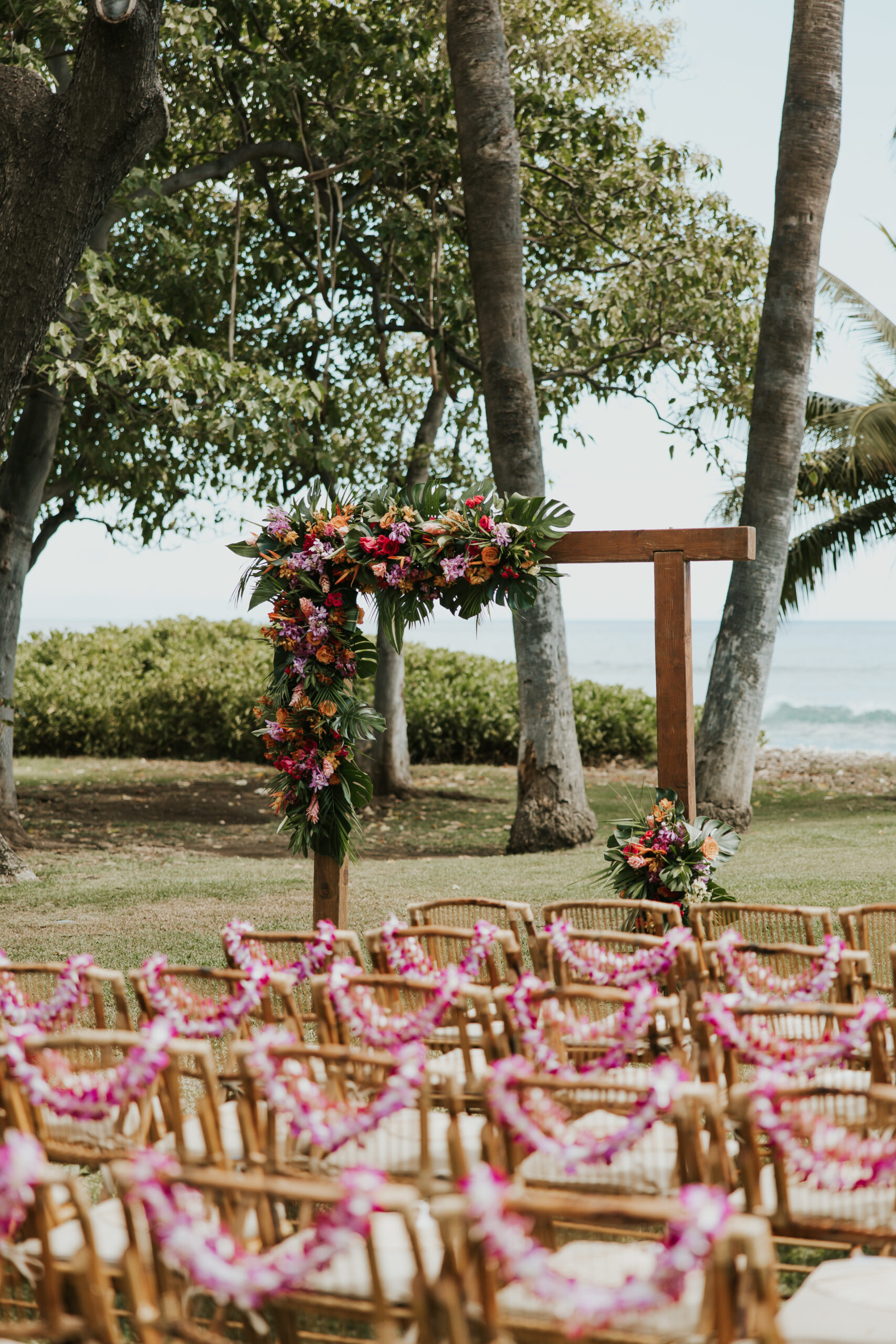 Wooden ceremony arch decorated with tropical florals, surrounded by bamboo chairs and ocean views at a dreamy Maui wedding venue.