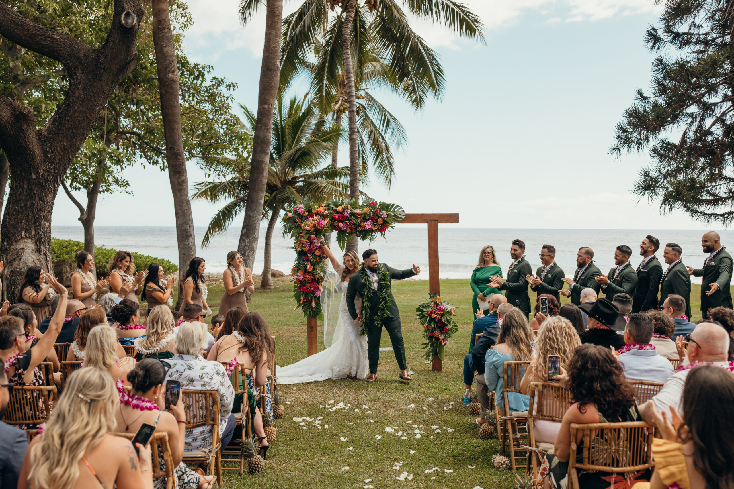 Bride and groom celebrate with raised arms as their guests cheer at the end of their ceremony at a vibrant Maui wedding venue.