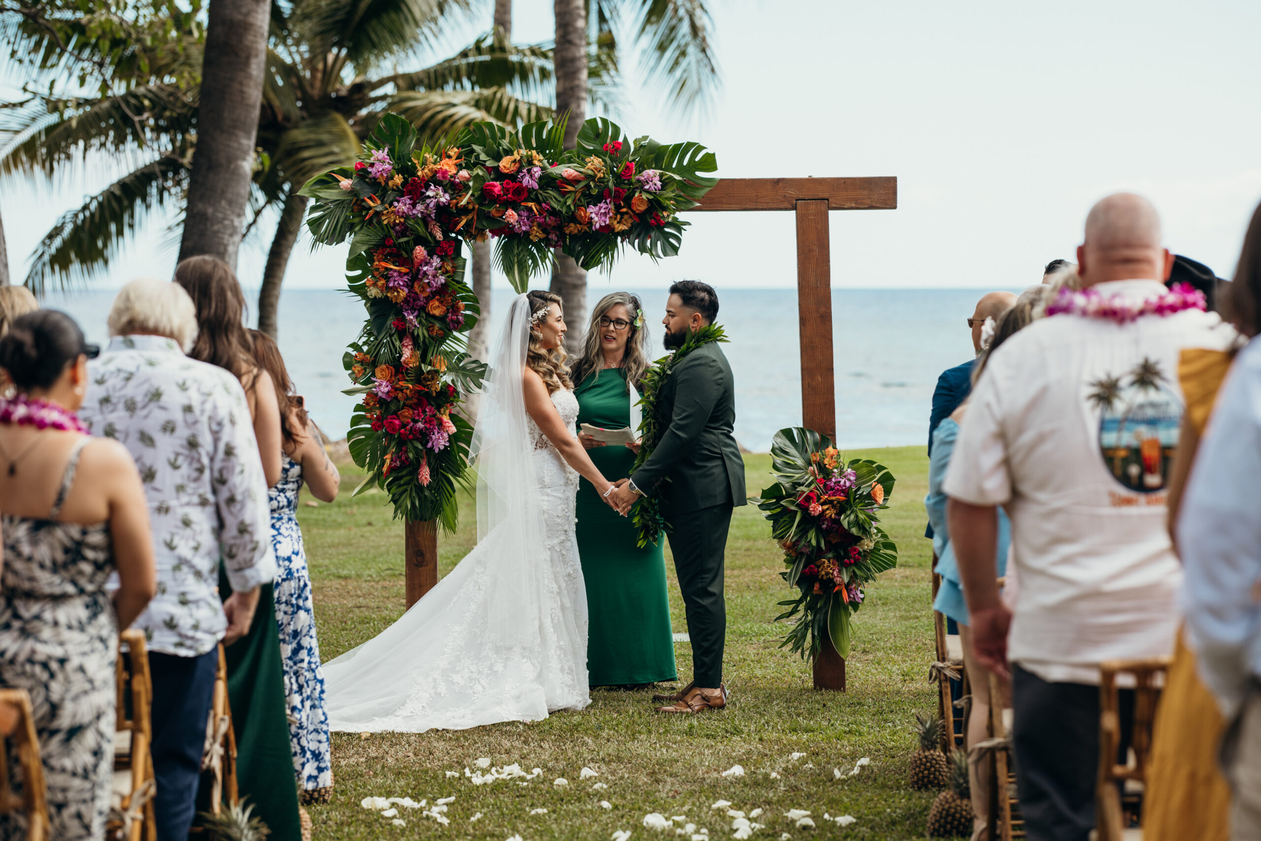 Couple holds hands under a tropical floral arch during their beachfront ceremony at a picture-perfect Maui wedding venue.