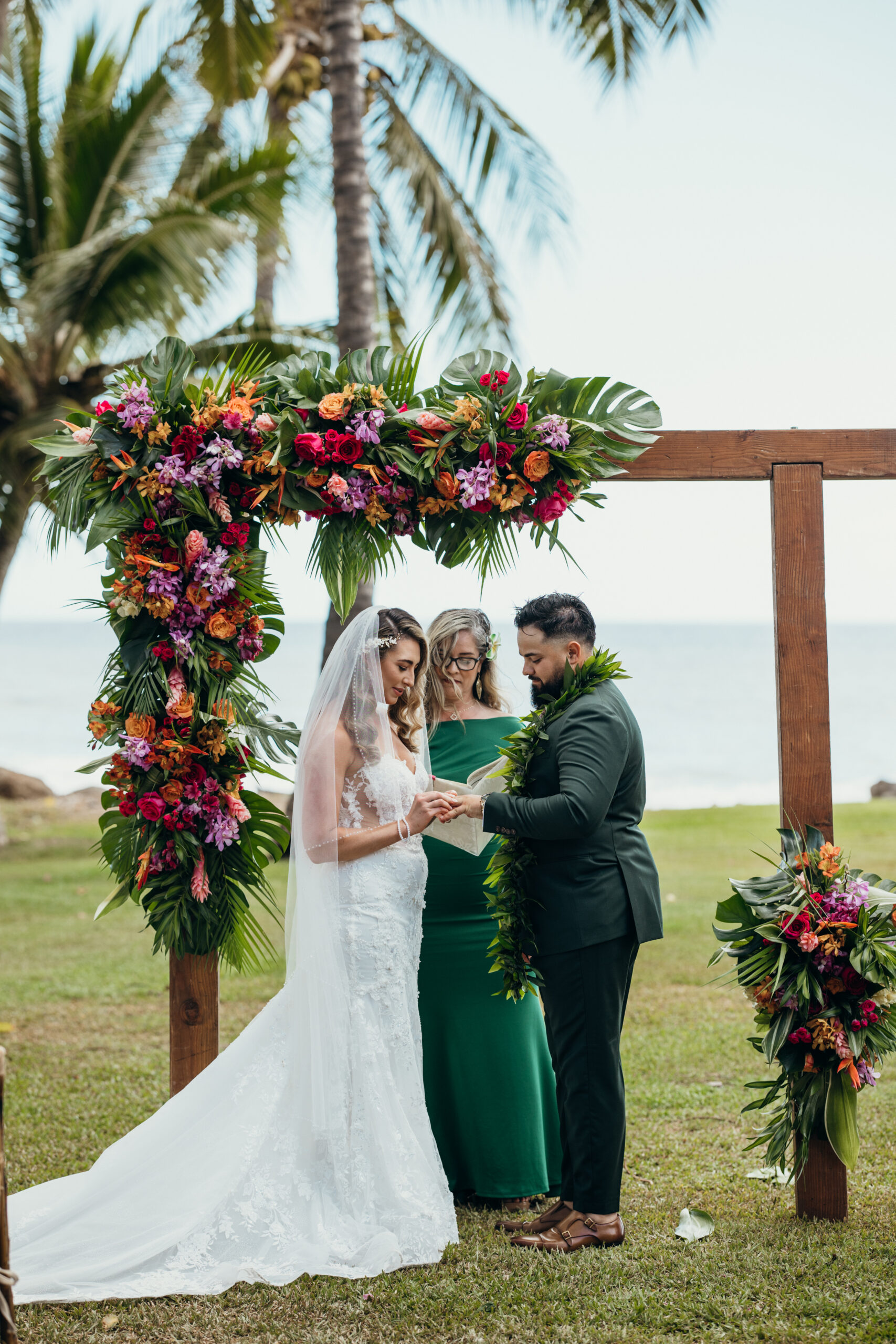 Bride and groom exchange rings during an intimate oceanfront ceremony, framed by palms and island blooms.
