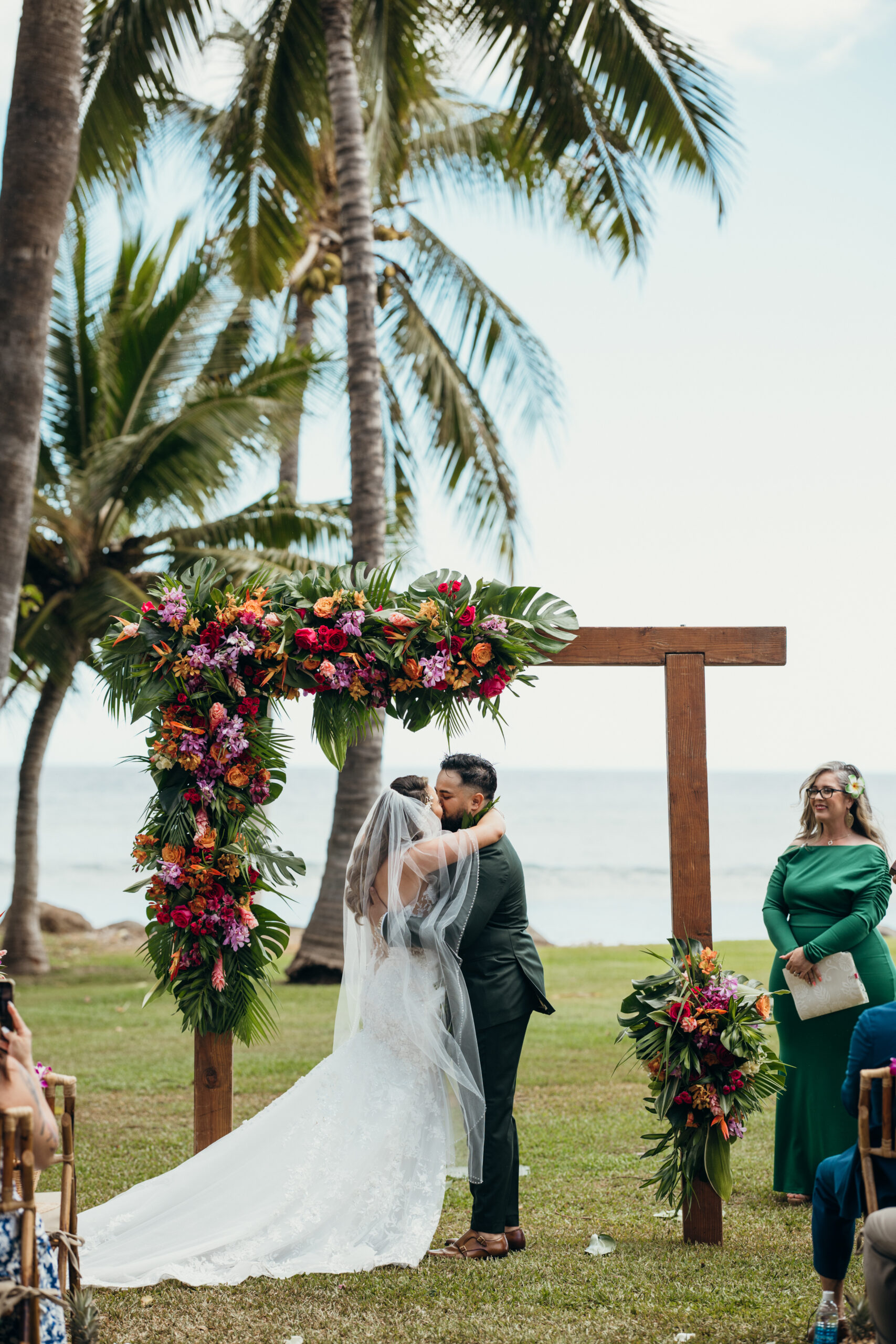 Bride and groom share their first kiss as a married couple under a vibrant floral arch at their Maui wedding venue.