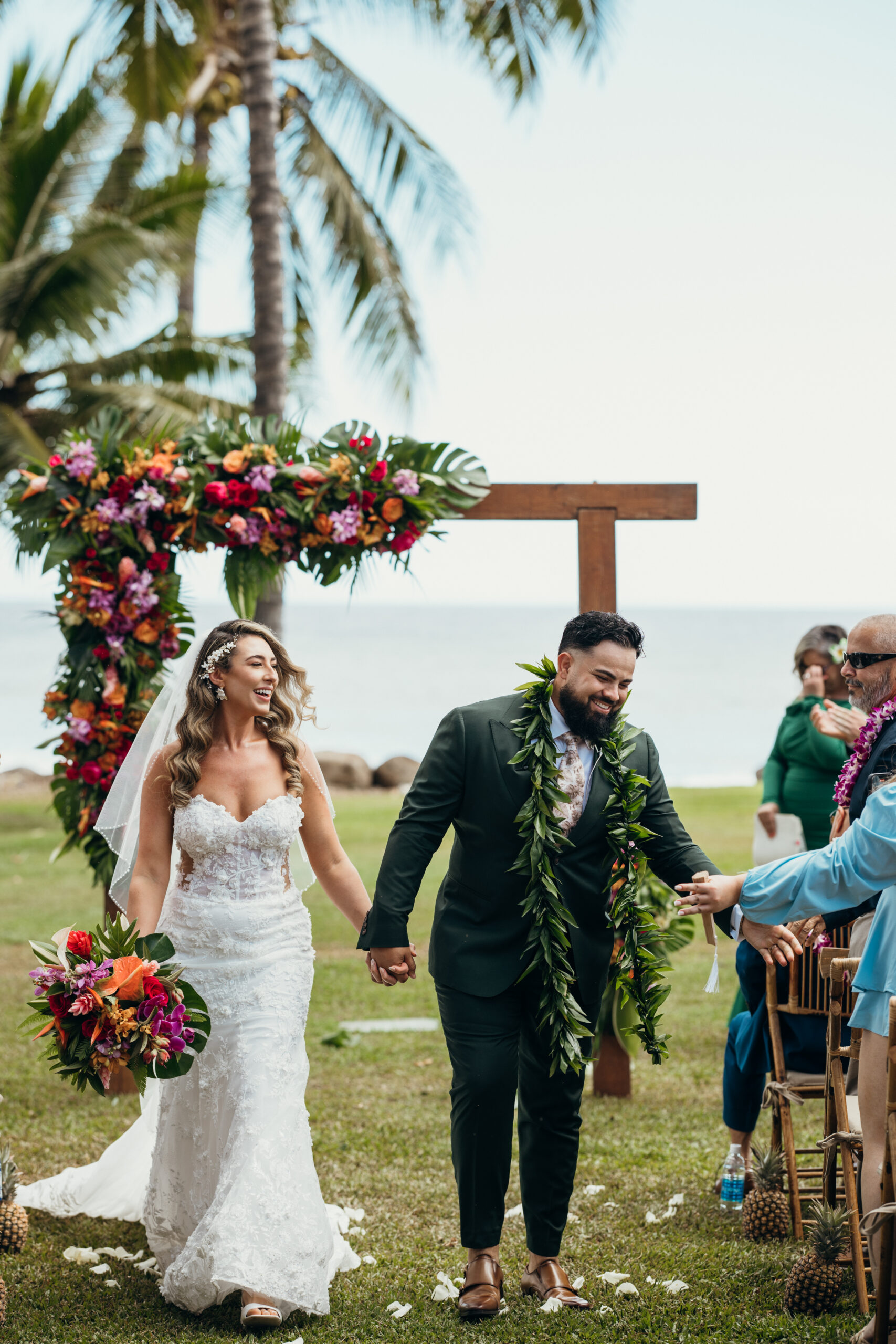 Just married! Bride and groom smile and hold hands walking back down the aisle with ocean views behind them.