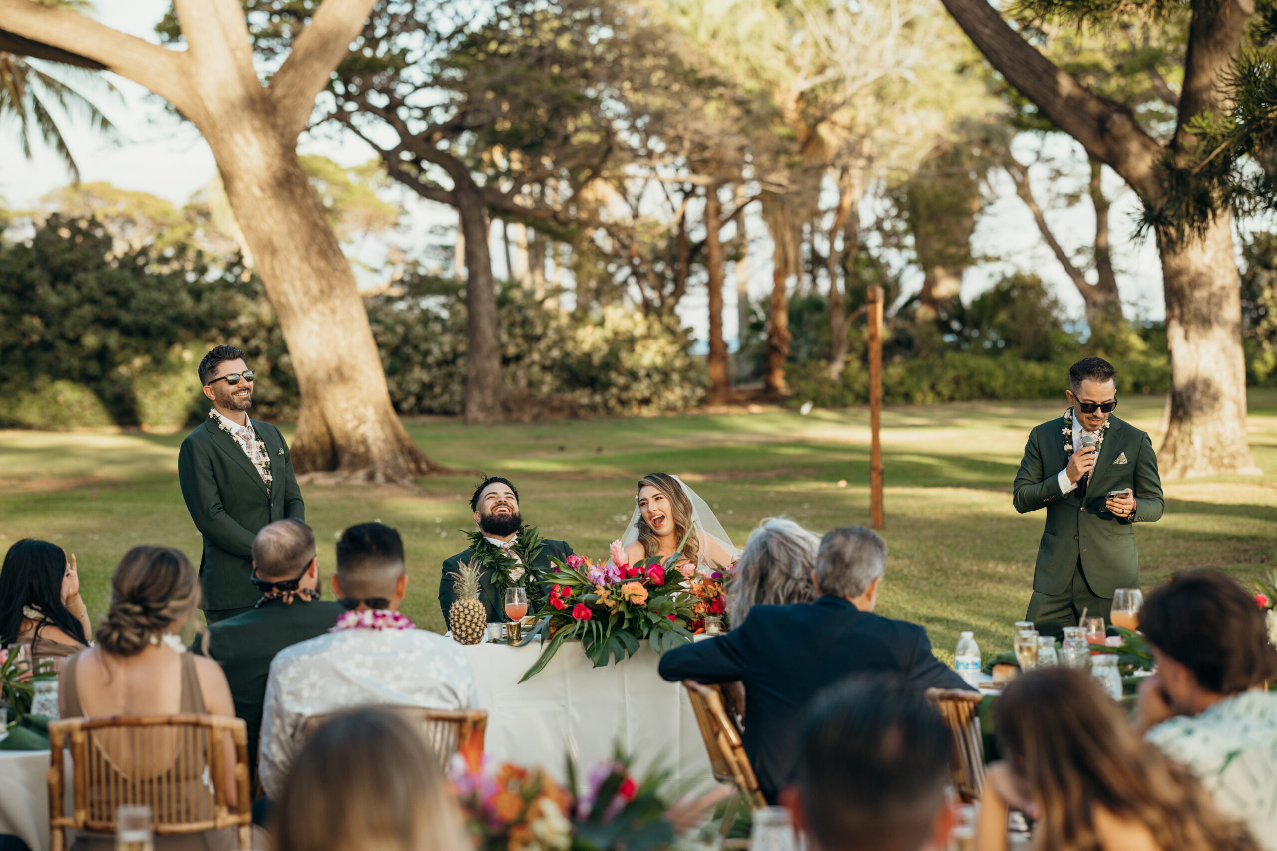 Candid moment during wedding speeches as the couple laughs with guests gathered under the trees at their Maui reception.