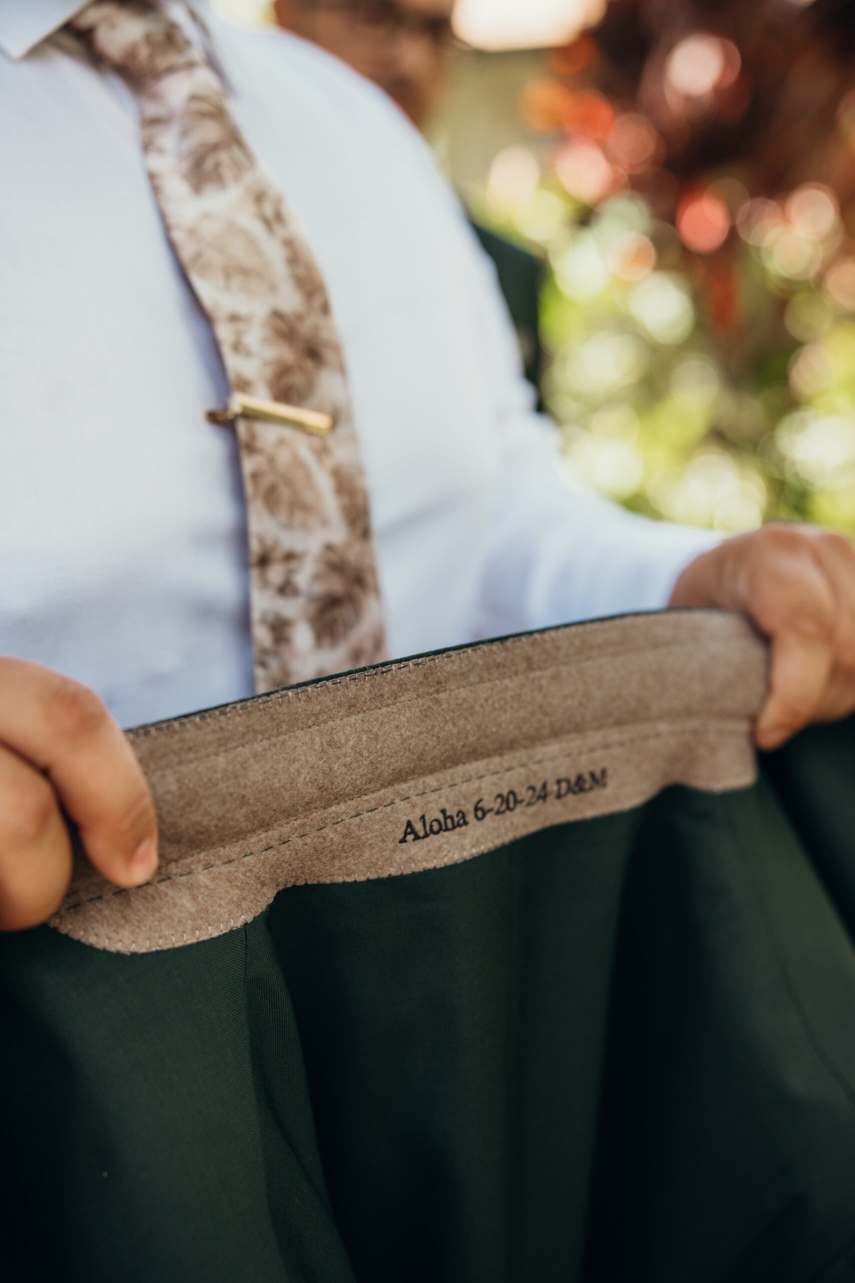 Groom holds open the lining of his suit jacket, revealing custom embroidery with their Maui wedding date and a sweet “Aloha” touch.