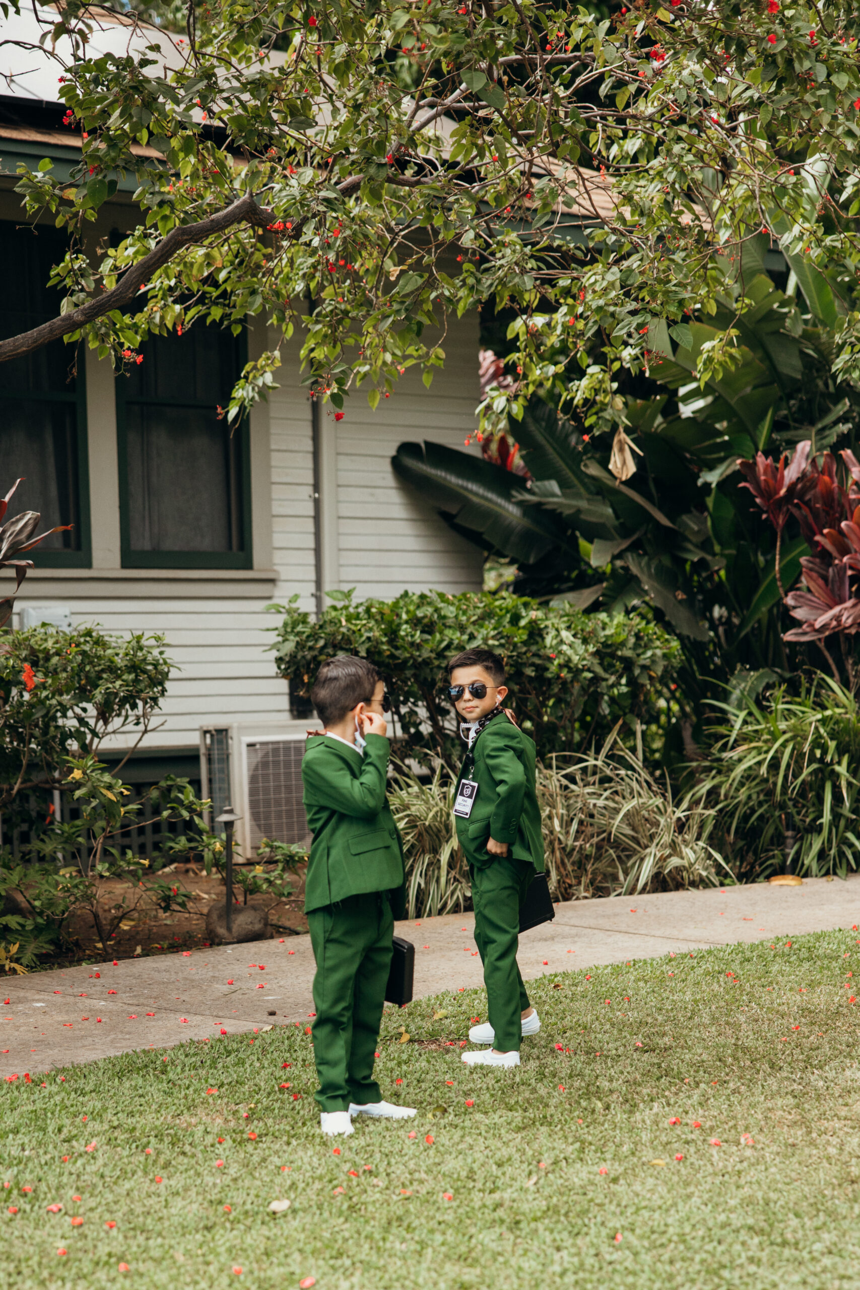Two boys in matching green suits stand under a blossoming tree, chatting before the wedding begins.