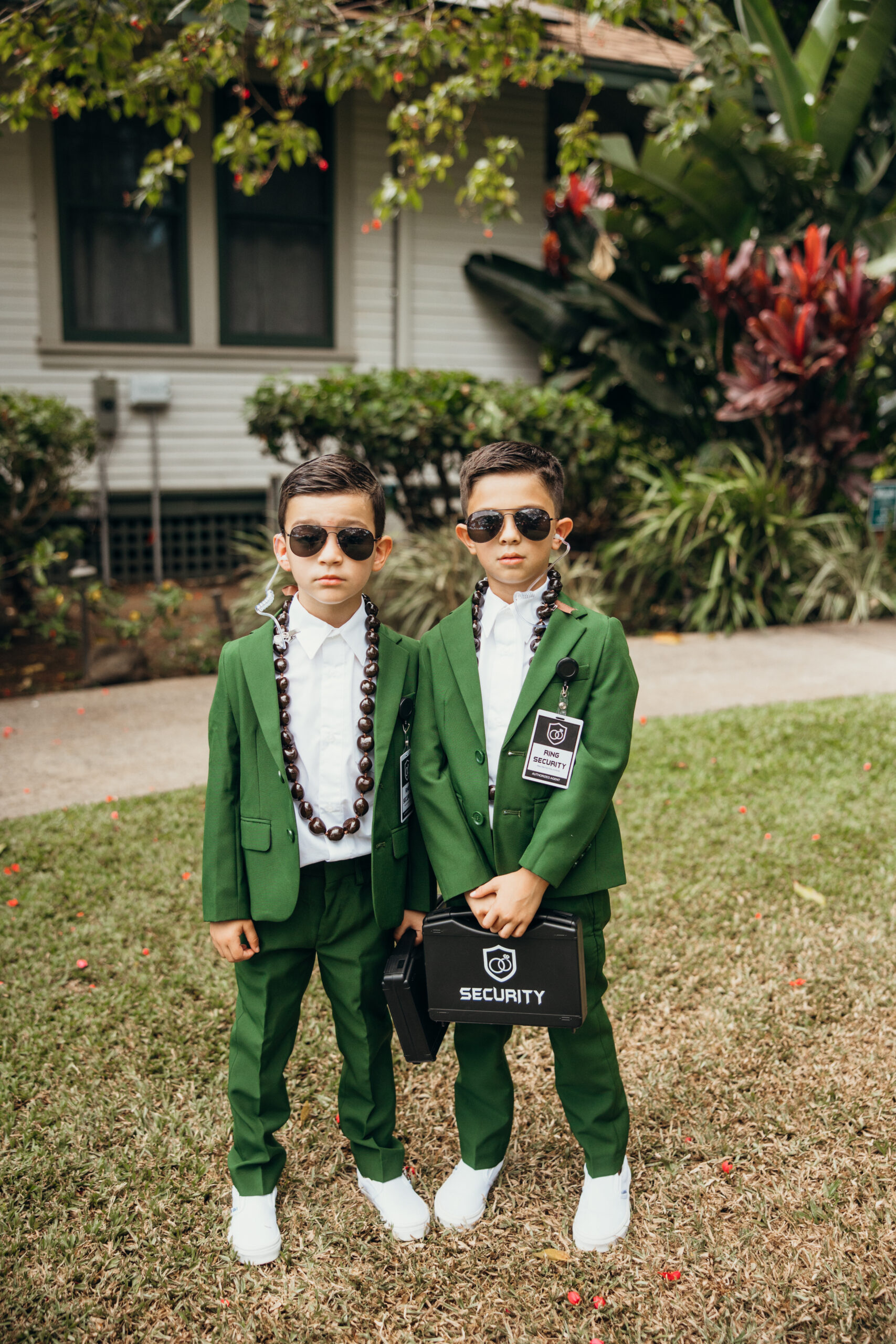 Ring bearers dressed as “wedding security” pose in green suits, sunglasses, and official briefcases—ready to protect the rings in style.