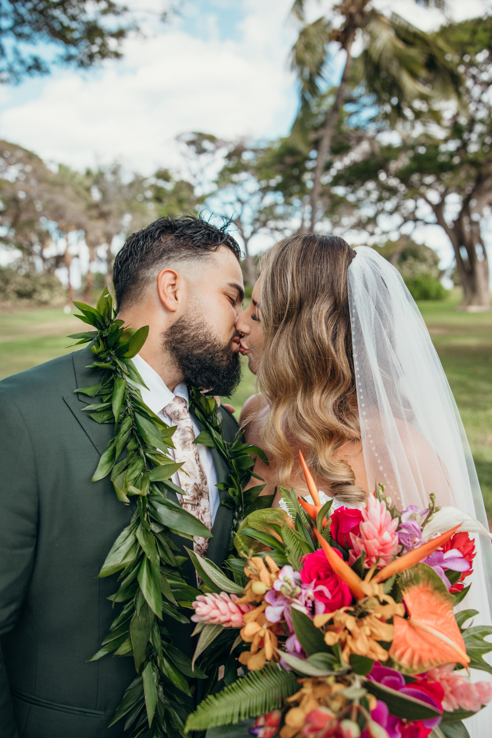 Close-up of the newlyweds sharing a kiss, framed by the bride’s vibrant bouquet and soft Hawaiian light.