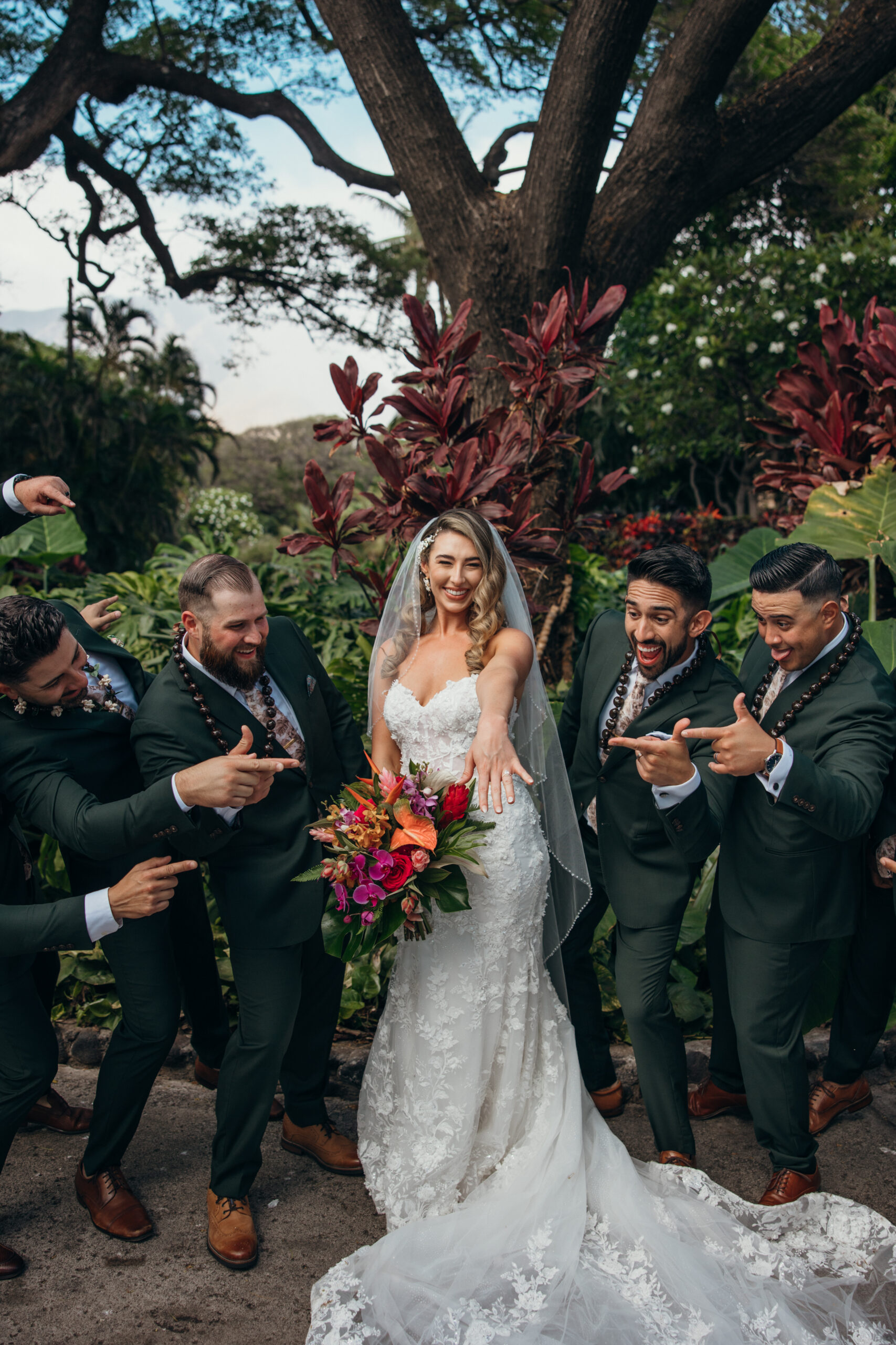 Bride showing off her ring with the groomsmen gathered around her, celebrating big smiles and island energy in a tropical garden.