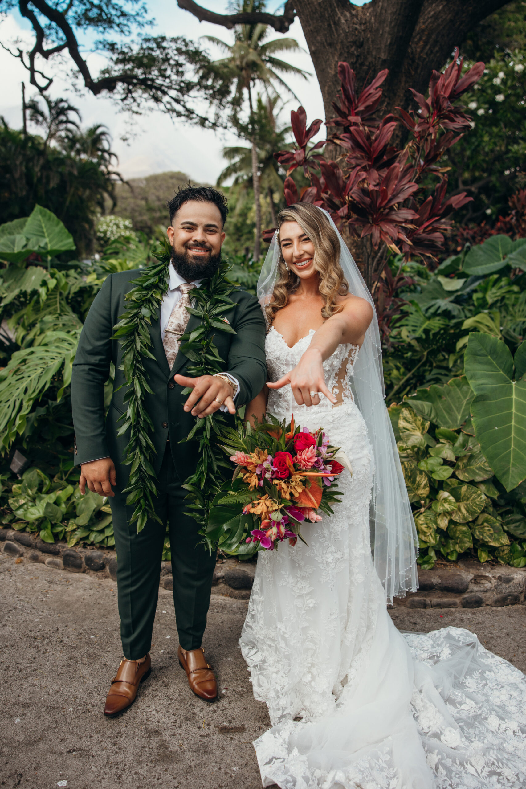 Joyful couple showing off their rings and bouquet, surrounded by tropical greenery in a vibrant garden setting.