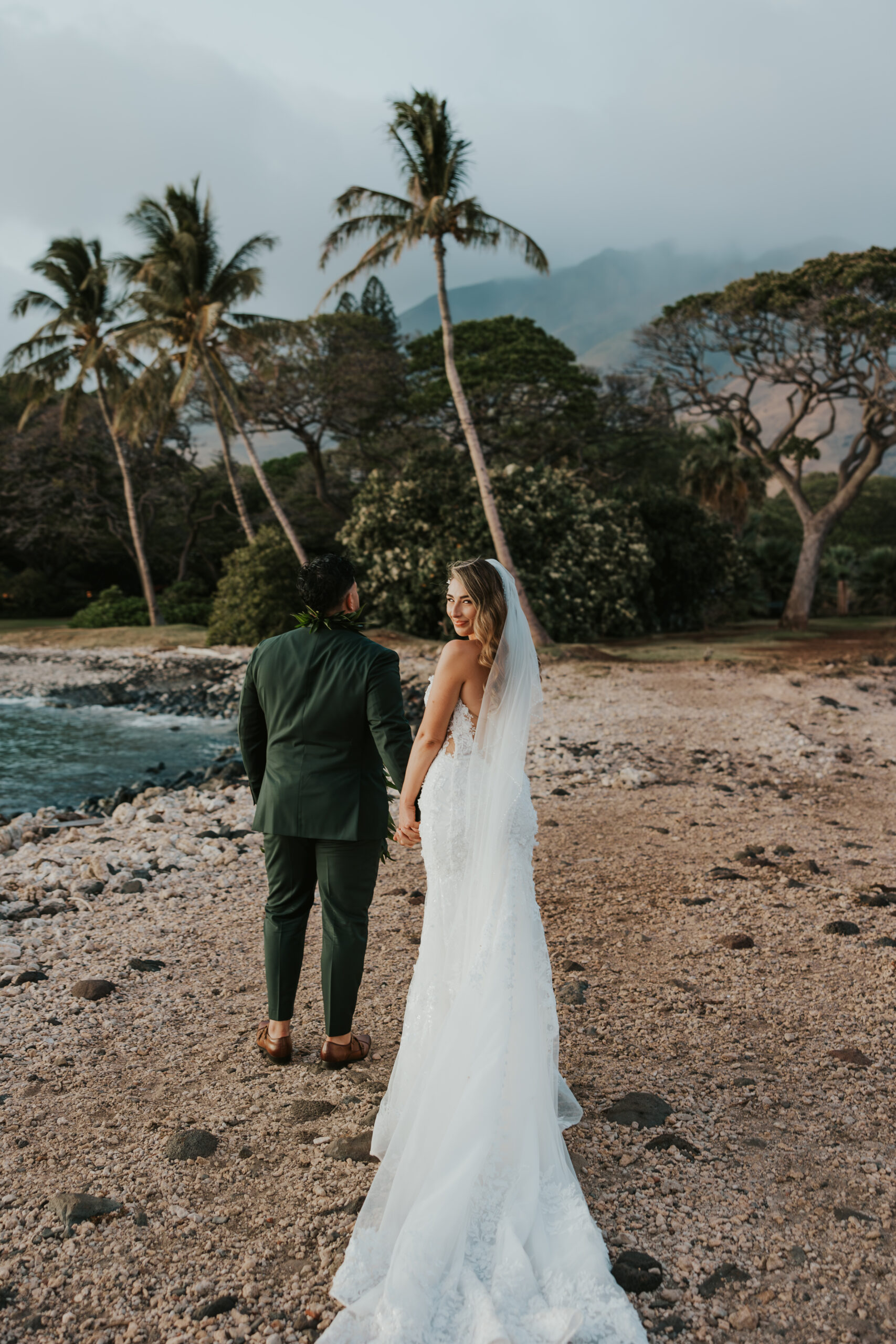 Bride holding groom's hand and looking over her shoulder during outdoor bridal portraits.