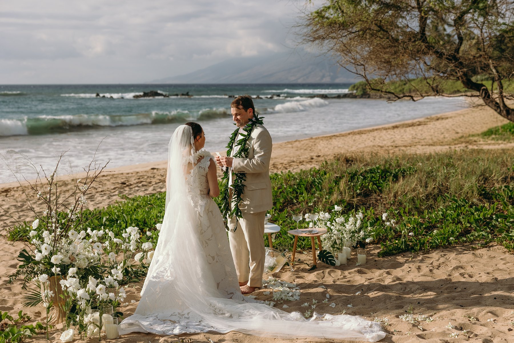 Bride and groom exchanging leis during a romantic Maui beach ceremony surrounded by white florals.