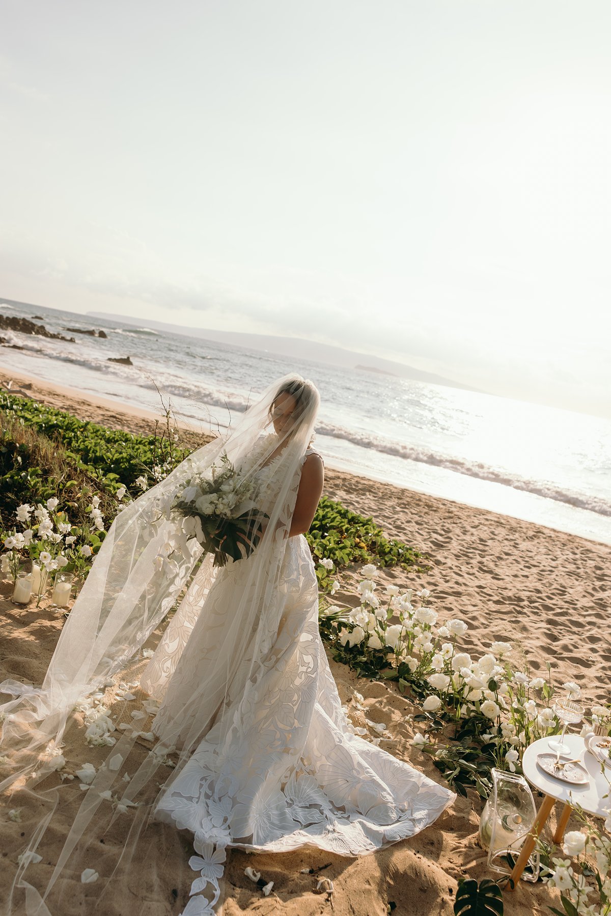Bride standing at Makena beach ceremony altar with veil flowing toward the ocean