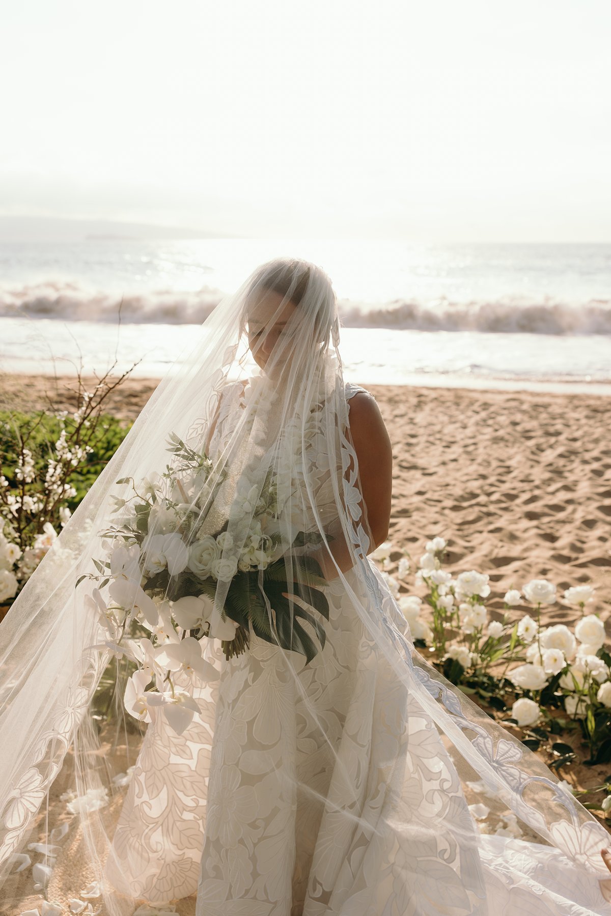 Bride standing with veil flowing in ocean breeze during a romantic Maui beach elopement moment