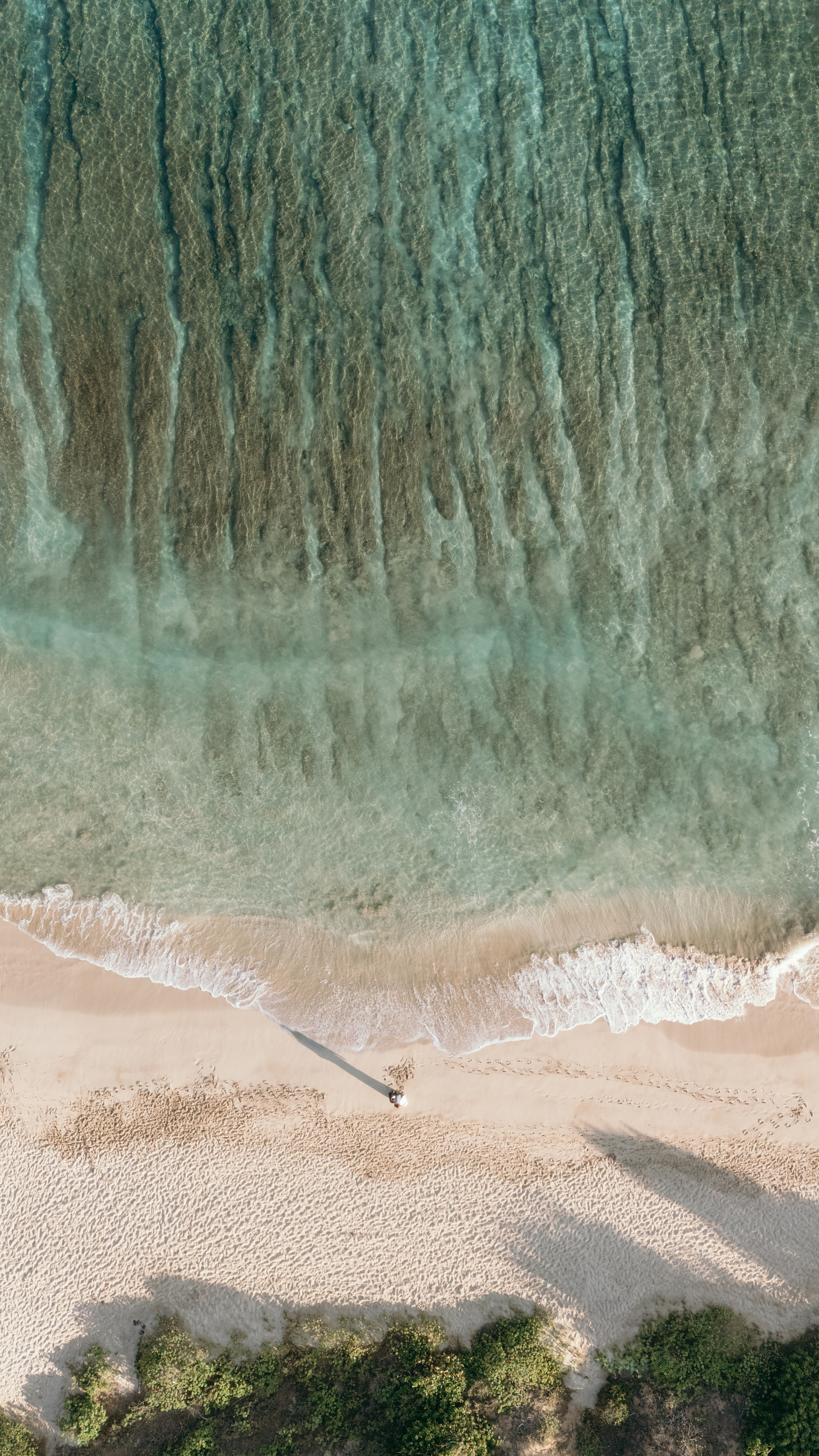 Top-down aerial view of gentle waves meeting a quiet Maui shoreline with a couple standing near the water, captured with drone videography.