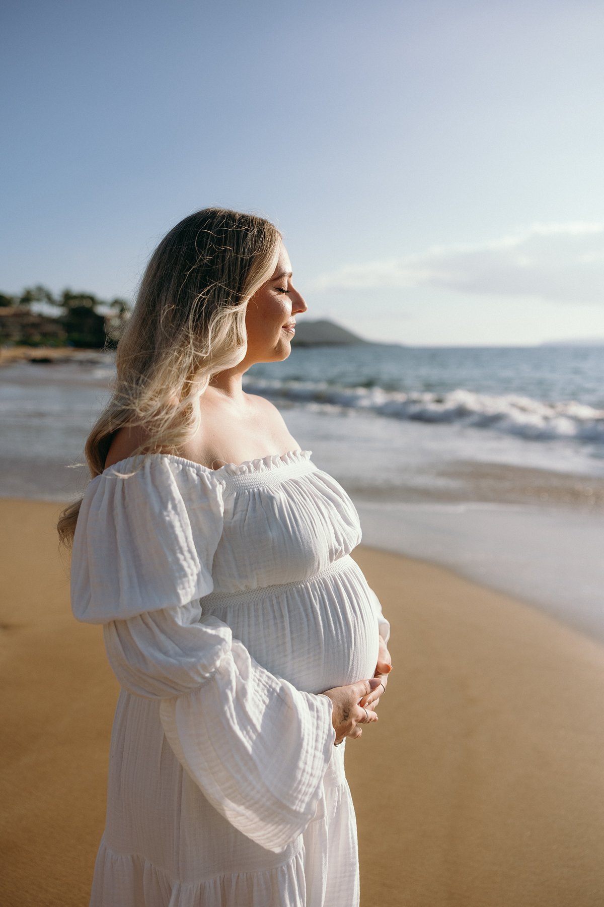 Expecting mother standing by the ocean at sunset during a peaceful Maui babymoon.