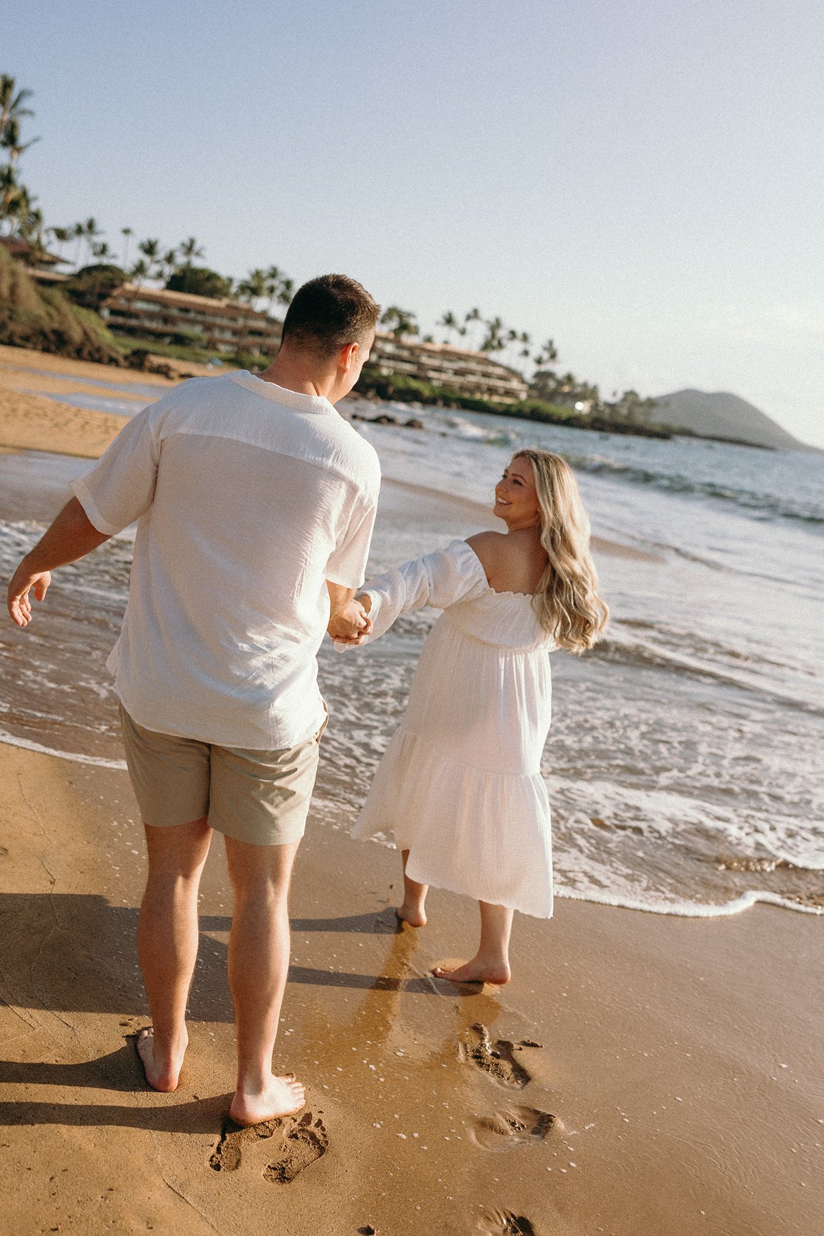Couple walking hand in hand along the shoreline during their Maui babymoon maternity session.