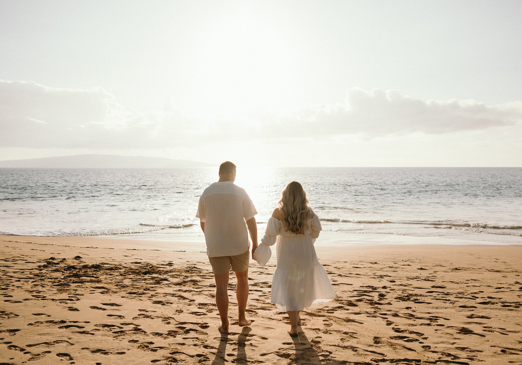 Expecting couple standing together in the ocean at sunset during a romantic Maui babymoon.