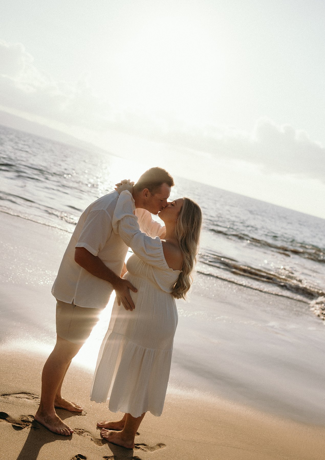 Couple kissing beside the ocean during golden hour maternity photos on a Maui babymoon.