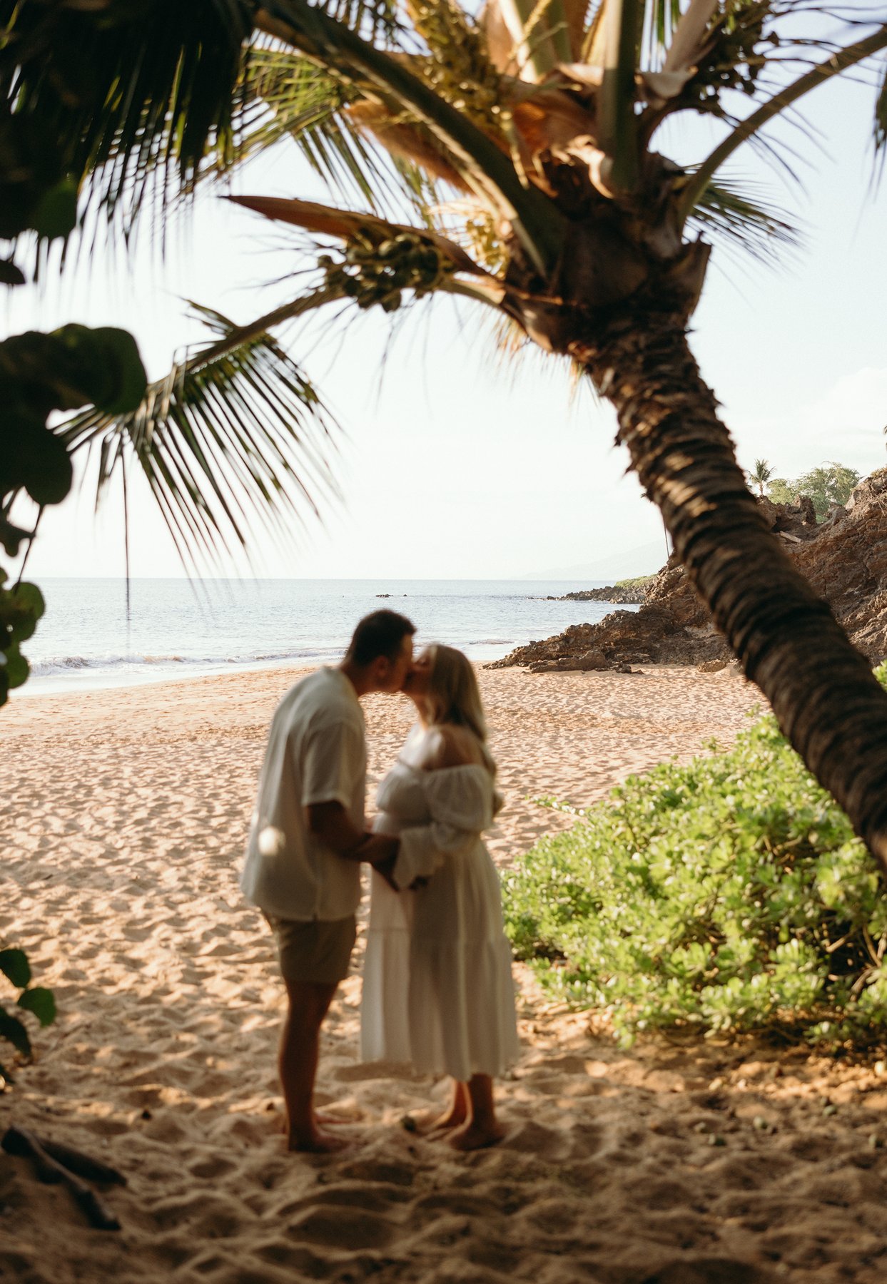 Pregnant couple holding hands in ocean waves during golden hour maternity photos in Maui.