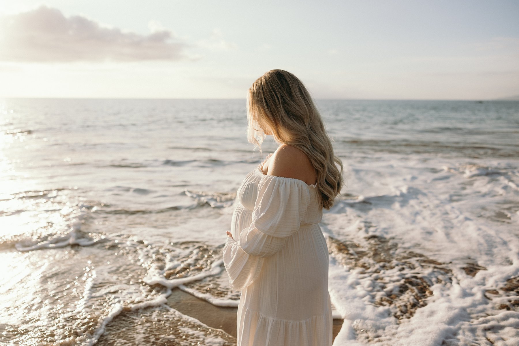 Expecting mother standing in the ocean at sunset during her Maui babymoon beach maternity photos.