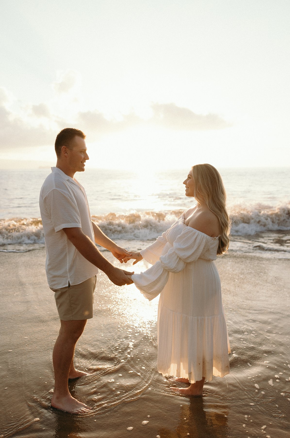 Expecting couple holding hands in the ocean at sunset during their Maui babymoon maternity photos.