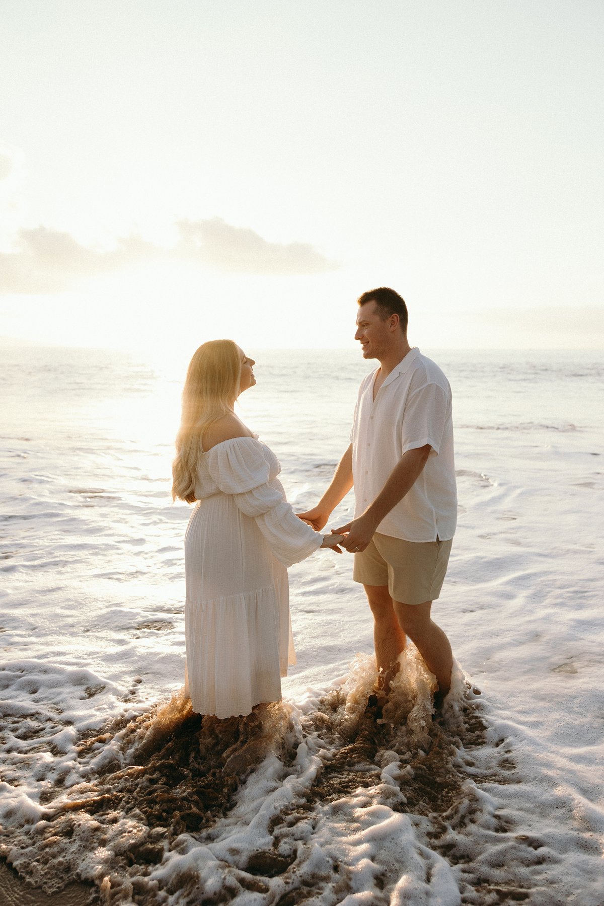 Expecting couple walking together through a tropical beach path surrounded by palm trees and greenery.