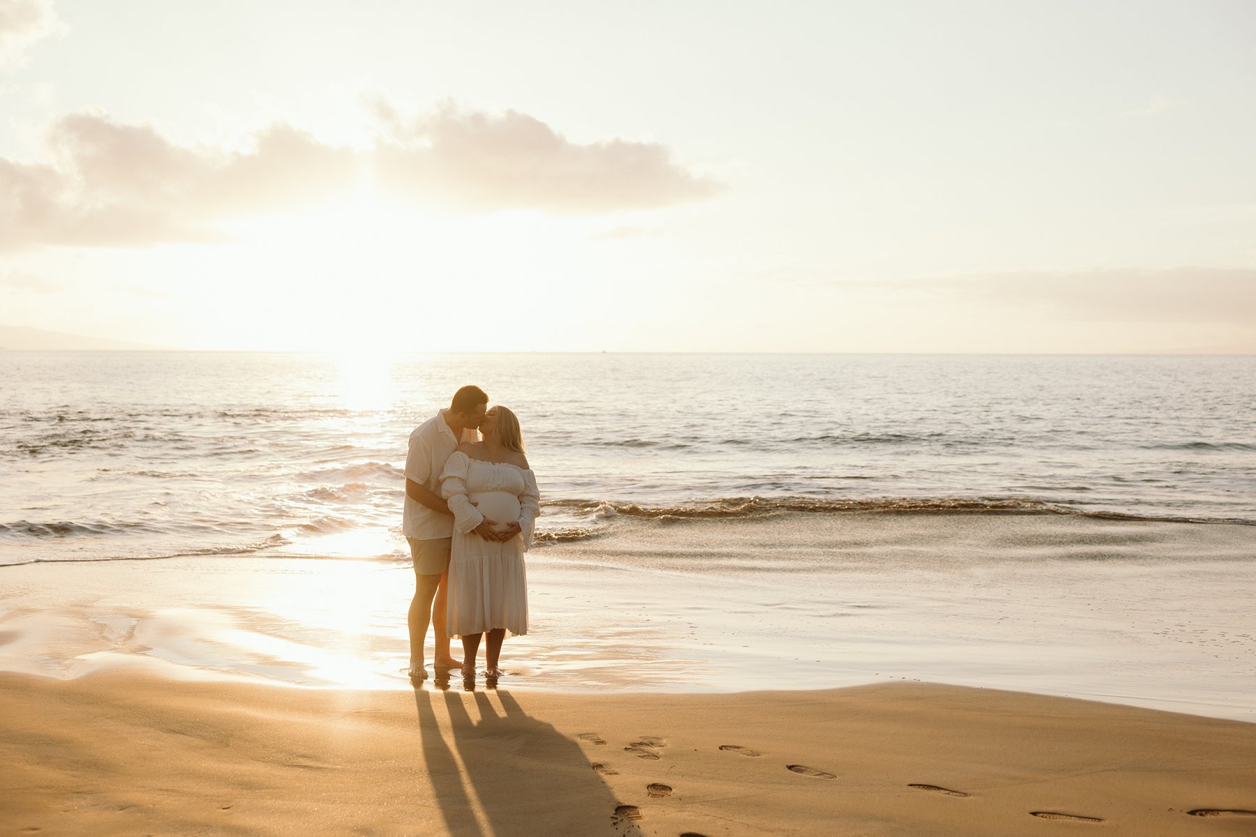 Expecting couple embracing at sunset along the shoreline during their Maui babymoon.
