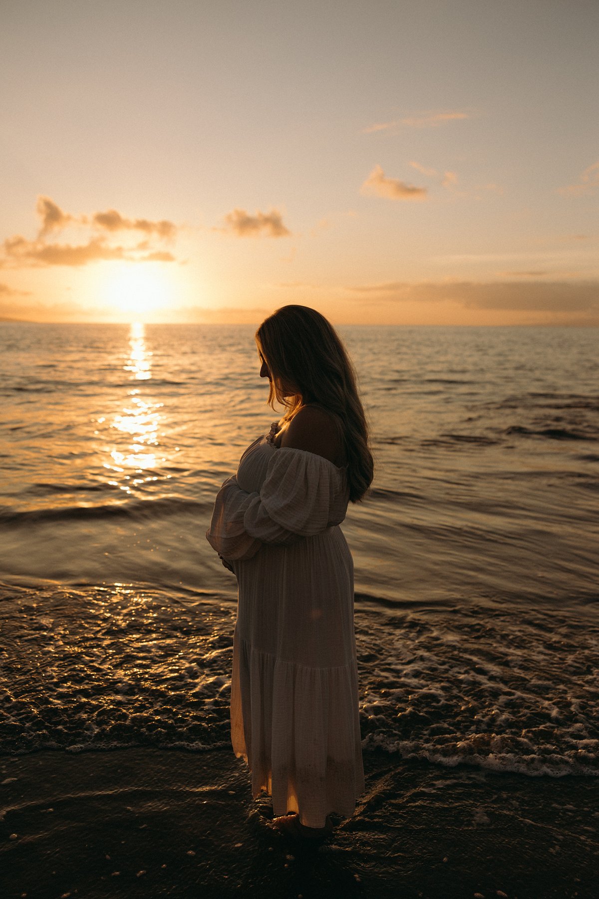 Pregnant woman standing in the ocean at golden hour during a peaceful Maui babymoon.