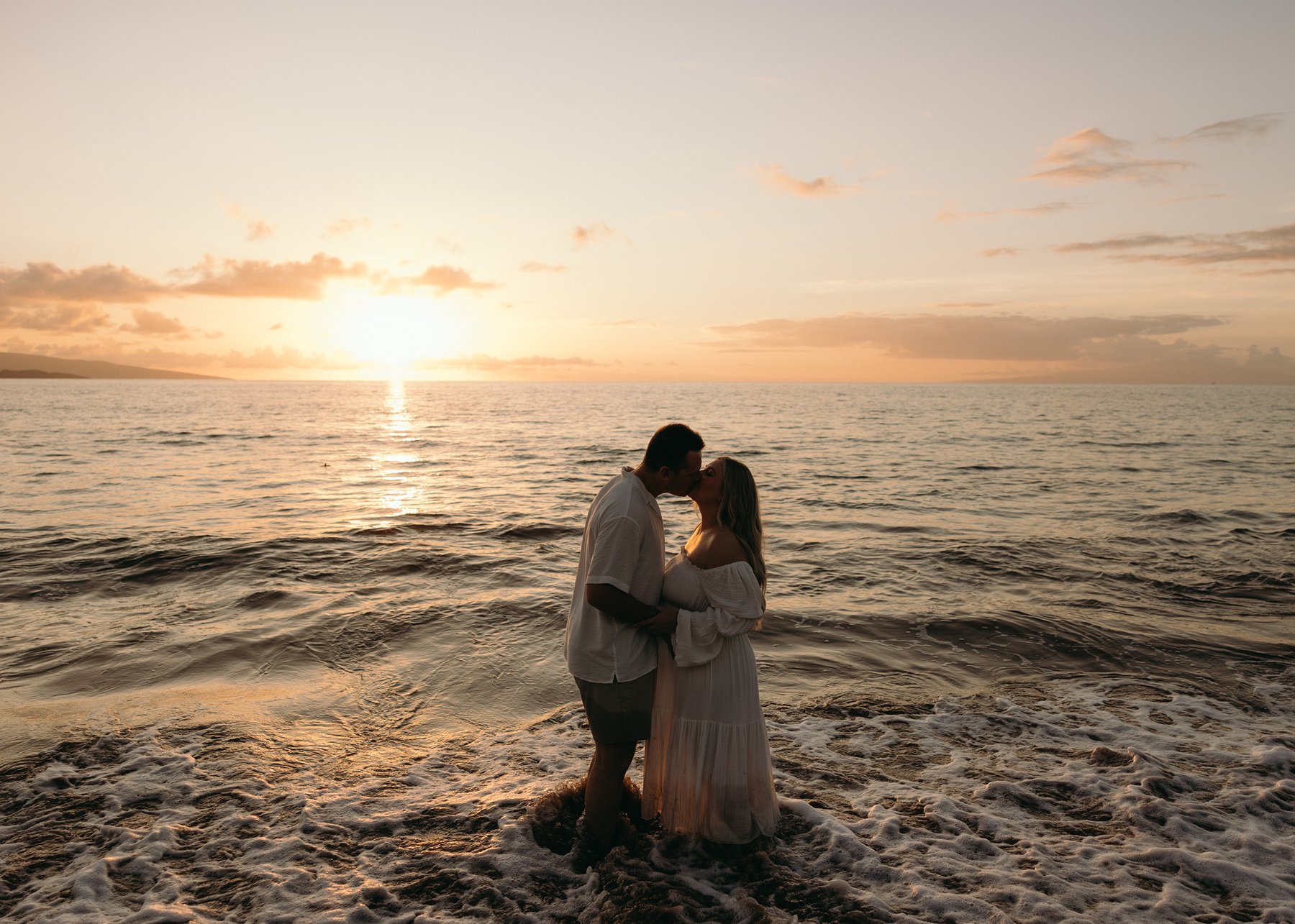 Couple embracing in the ocean at sunset during a romantic Maui babymoon maternity session.