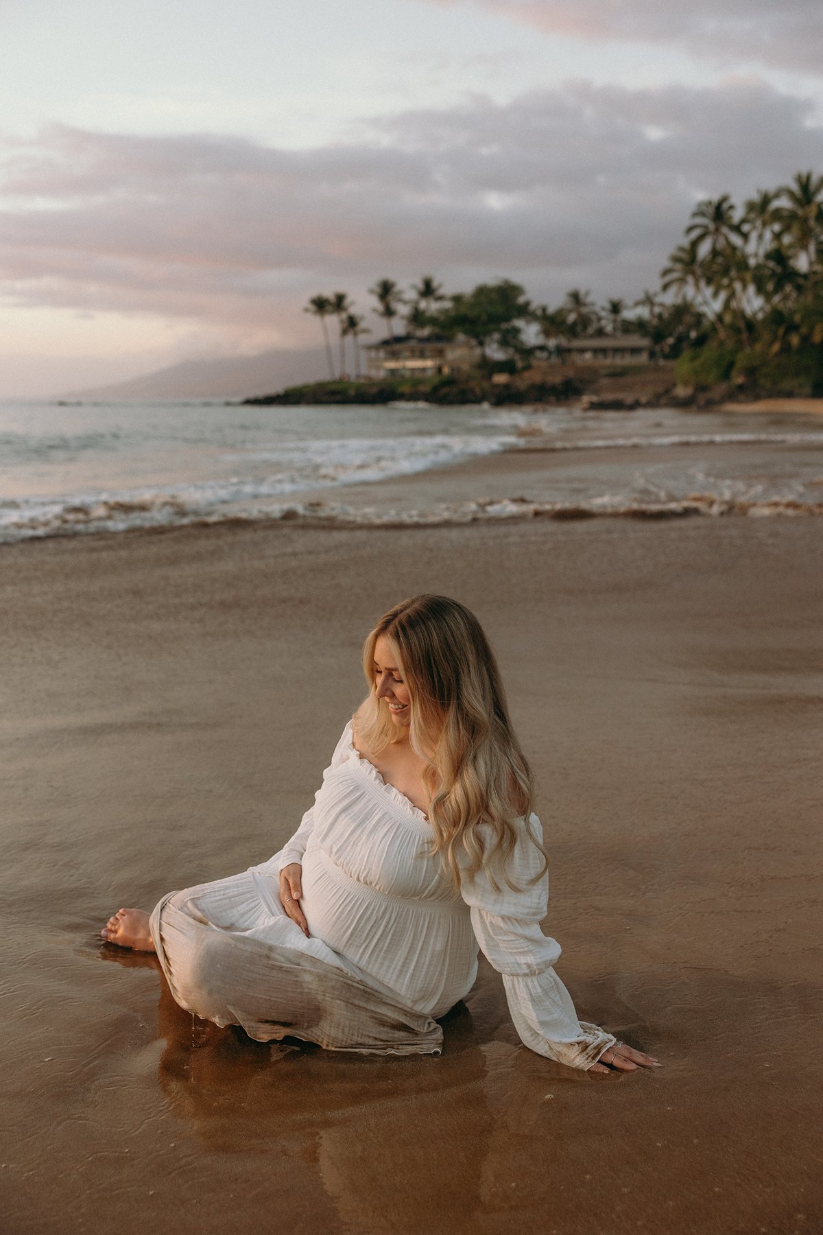 Expecting couple kissing beneath palm trees on a secluded Maui beach during their Maui babymoon.