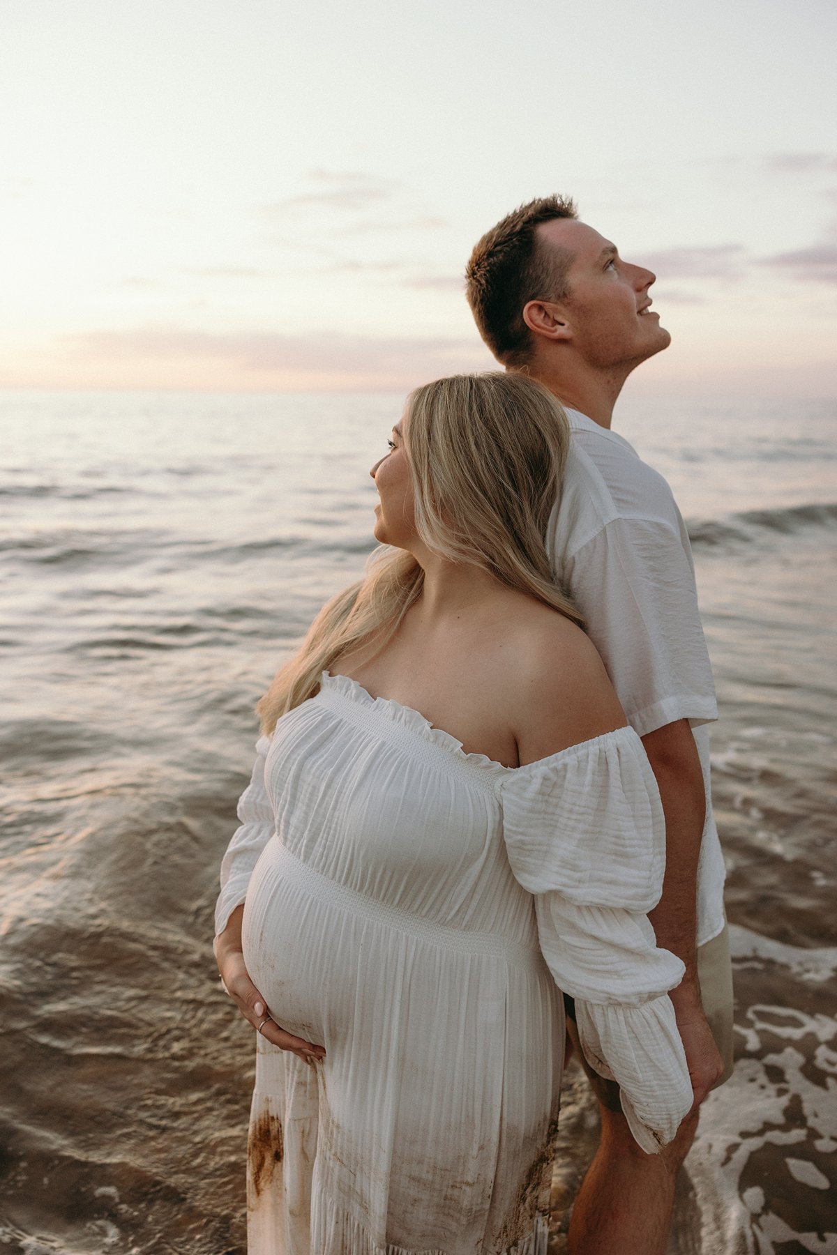Pregnant couple posing on lava rocks with palm trees behind them during a beach maternity session in Maui.