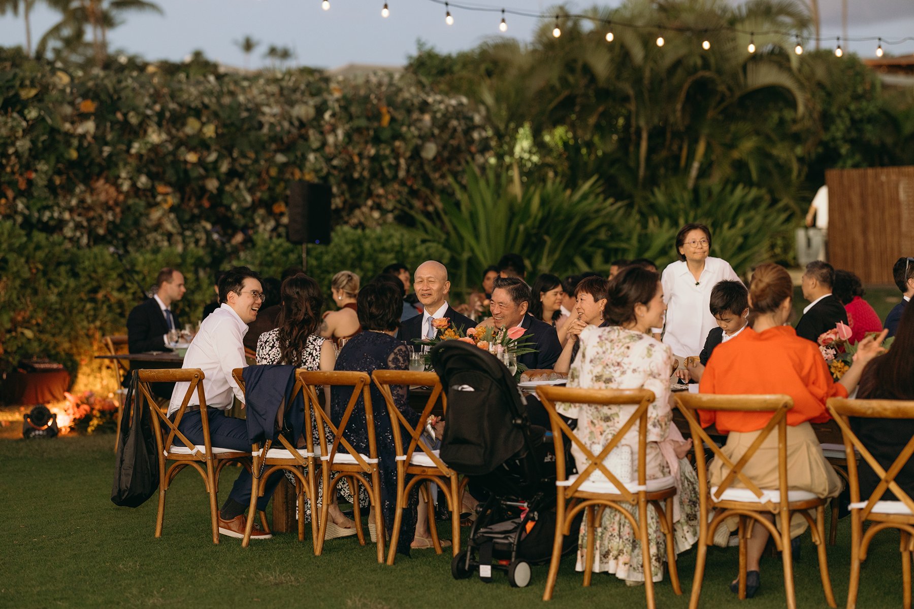 Wedding guests seated at long tables during outdoor reception at Maui resort wedding venue with string lights and tropical greenery