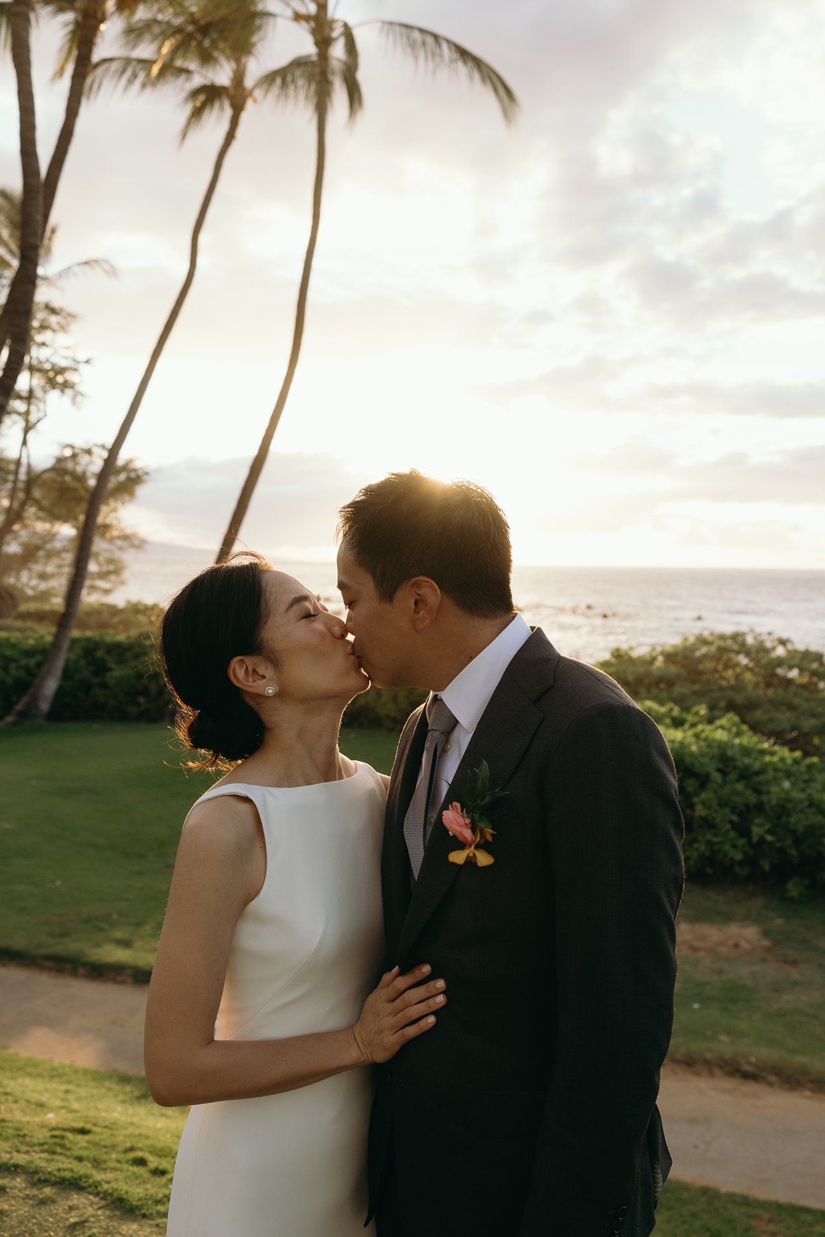 Bride and groom kissing with golden sunset light and ocean view in Hawaii