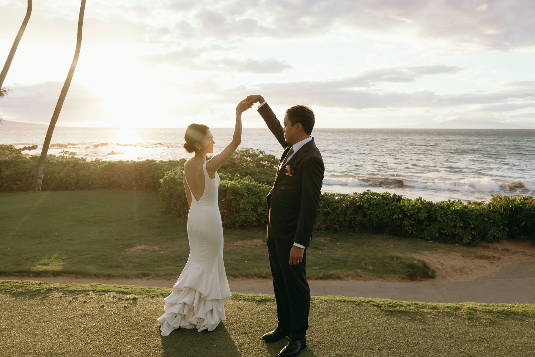 Bride and groom dancing at sunset overlooking ocean at Hawaii resort wedding venue