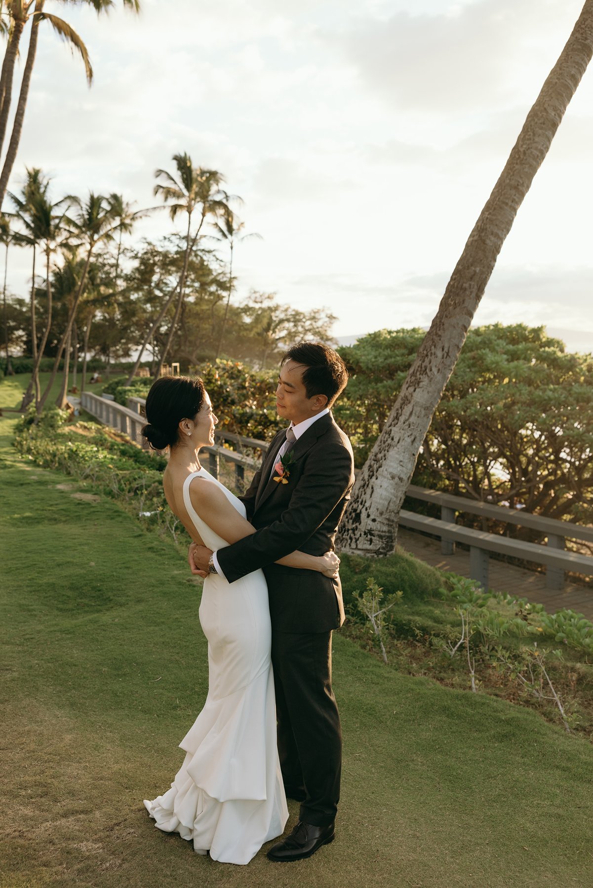 Bride and groom embracing on oceanfront lawn at Maui resort wedding venue during golden hour