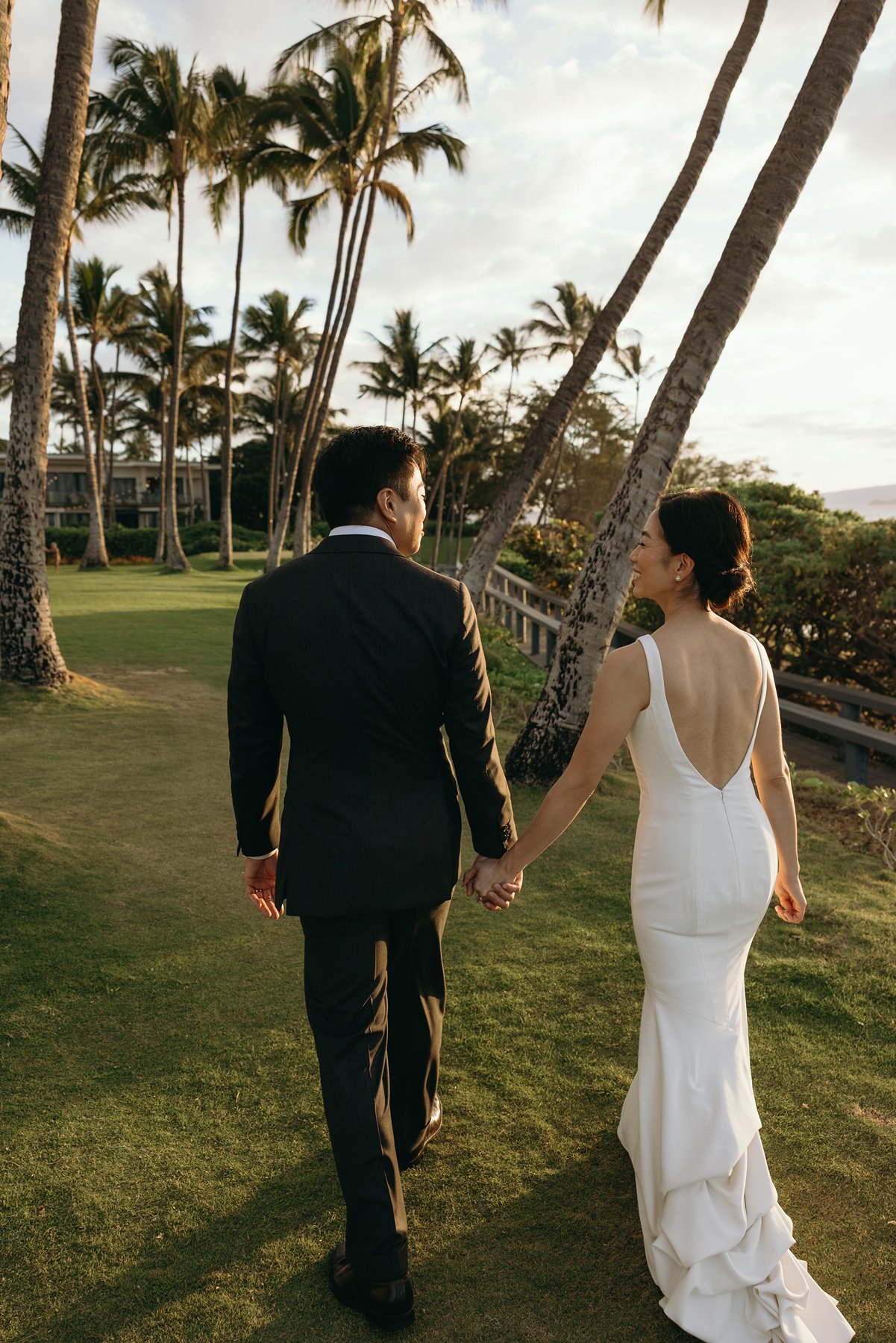 Newlywed couple walking hand in hand under palm trees at Maui destination wedding