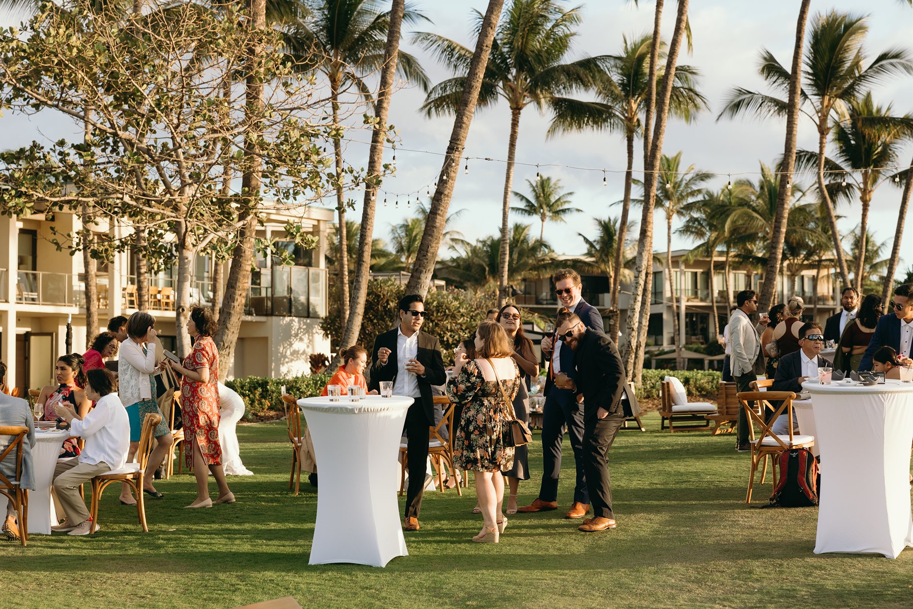 Wedding guests mingling during cocktail hour on lawn at Maui resort wedding venue with palm trees and villas